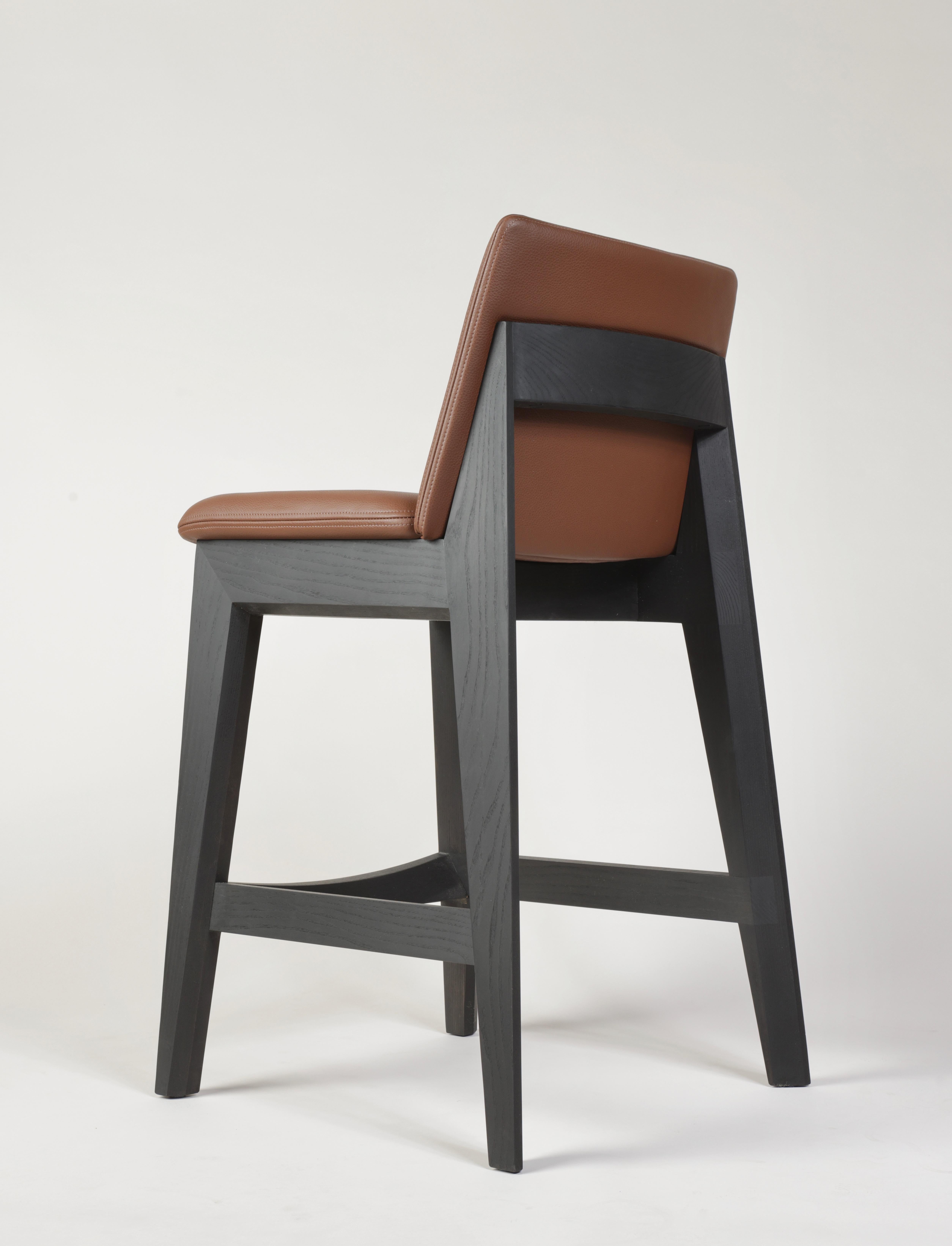Kroft counter stool shown in solid Blackened Ash & pebble grain leather upholstery. A contemporary stool with a smaller footprint and ample comfort. Functional joinery creates visual interest - angled profiles lend an overall lightness to the look.