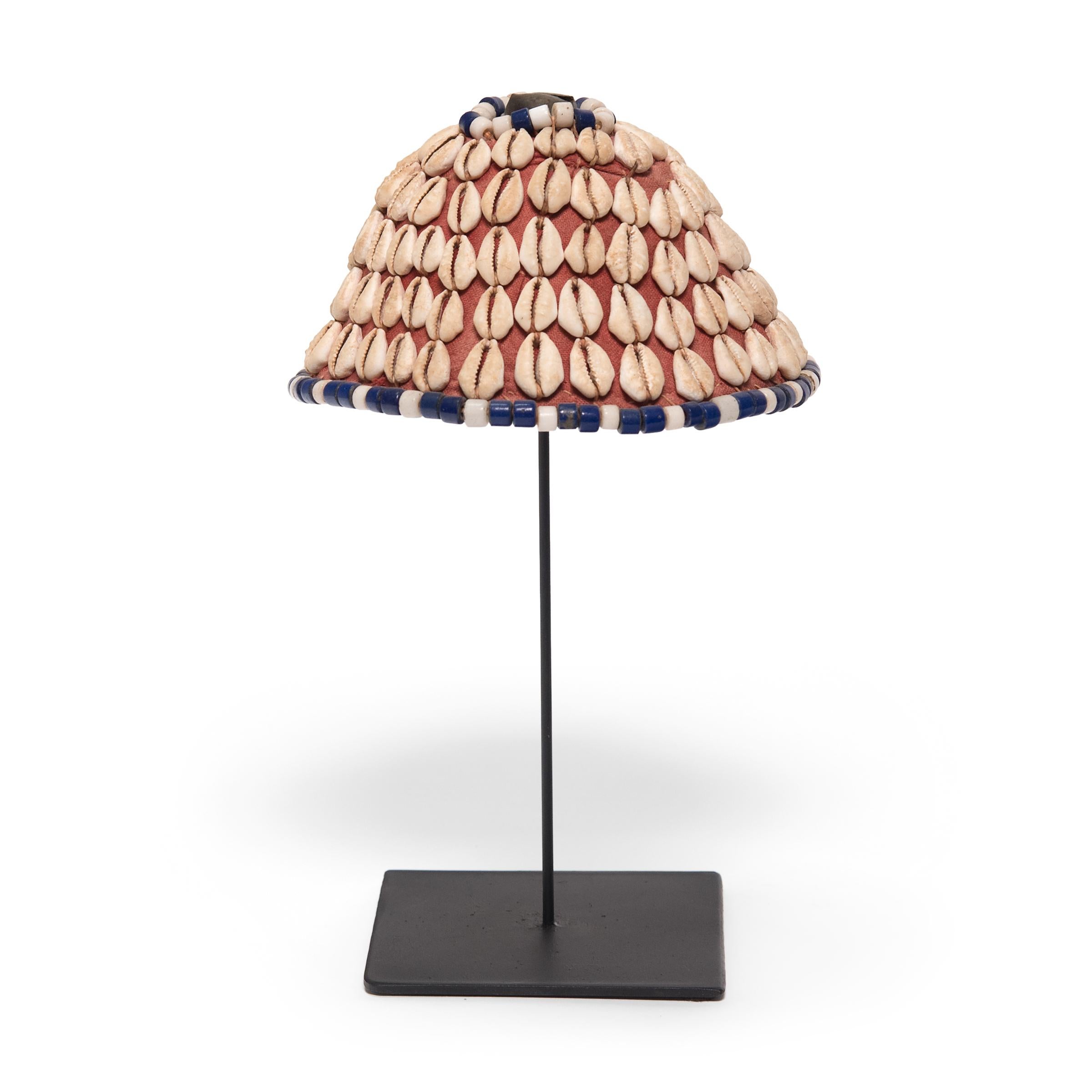 This petite cone-shaped cap, known as laket, was created by an artisan of the Kuba peoples of the Democratic Republic of the Congo. The base is made of a simple woven raffia fabric, which was then embellished with a pattern of cowrie shells and