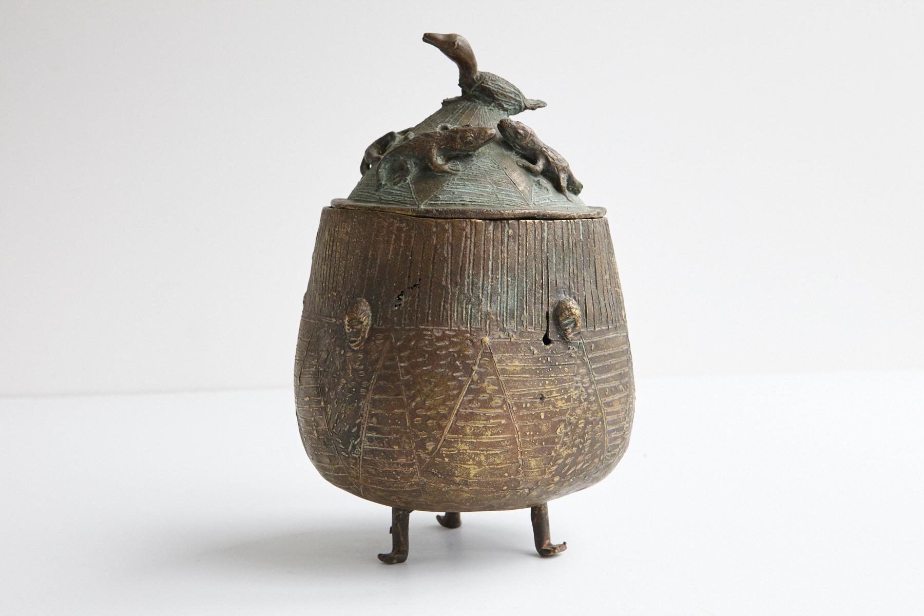 A beautiful bronze vessel, lidded pot on three legs, made by the Asante People, Ghana. Nicely cast lid with 4 reptiles and a bird. Several faces are depicted on the side of the vessel.
The so-called 