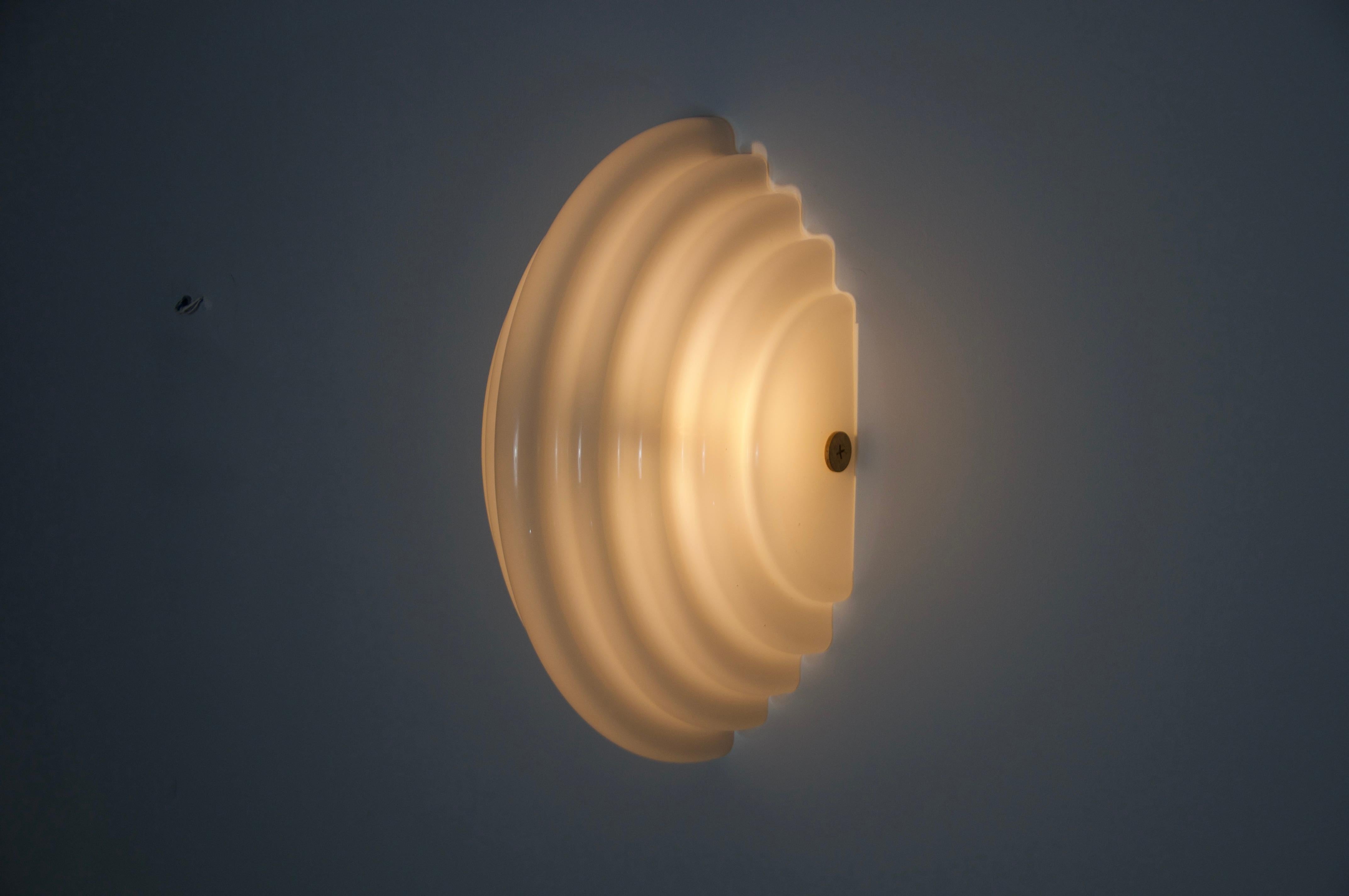 Diese auffällige Wandleuchte, die Kazuhide Takahama in den 1980er Jahren für Sirrah entwarf, ist ein perfektes Beispiel für minimalistisches und skulpturales Lichtdesign. Die halbkreisförmige Form aus geschichtetem Kunststoff und Acrylglas erzeugt