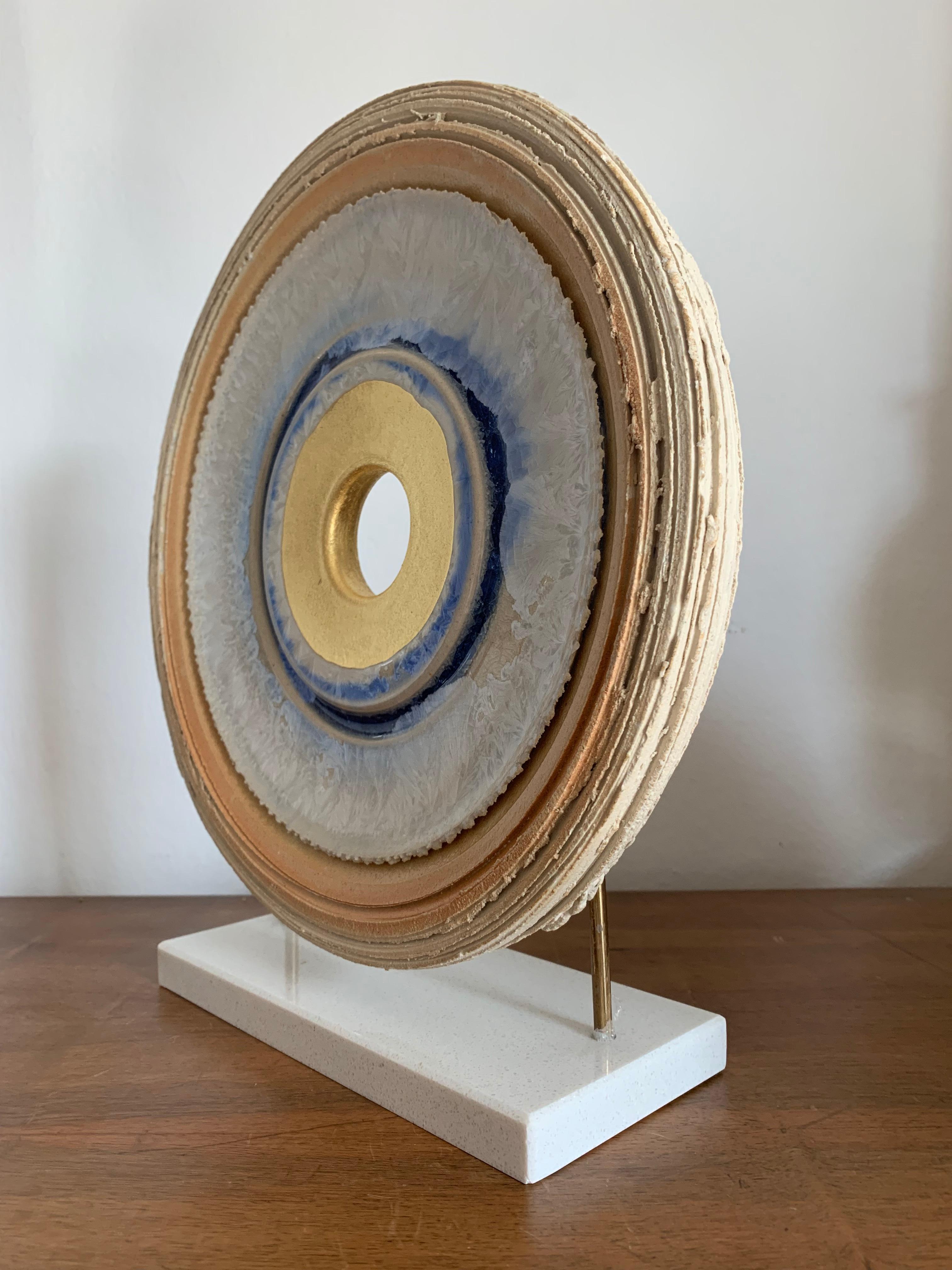 Questa bellissima scultura circolare contemporanea realizzata in ceramica con smalto di cristallo e foglia d'oro 24k poggia su un'elegante base di granito bianco.
Si tratta di un pezzo senza tempo, ricco di dettagli dovuti al processo di combustione