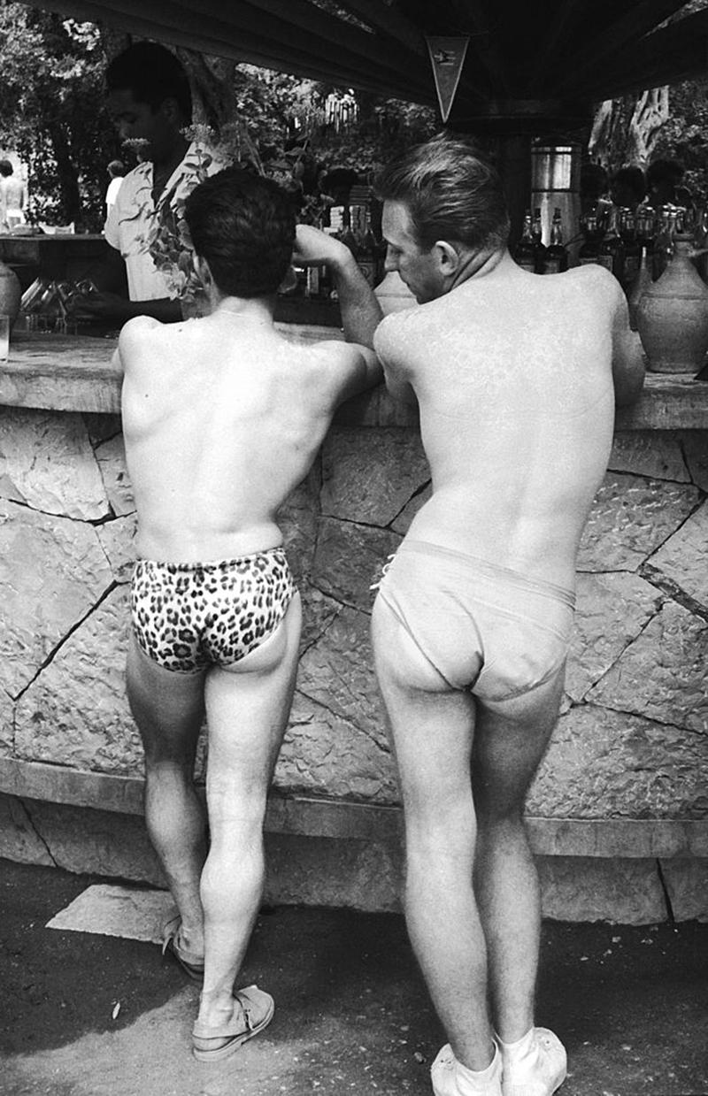 Cheeky Briefs by Kurt Hutton

A badly sun-burned holidaymaker admires his friend's leopard-print briefs, while standing at the bar of a holiday camp on Corfu. Original Publication: Picture Post - 7364 - A Place in the Sun for You - pub.