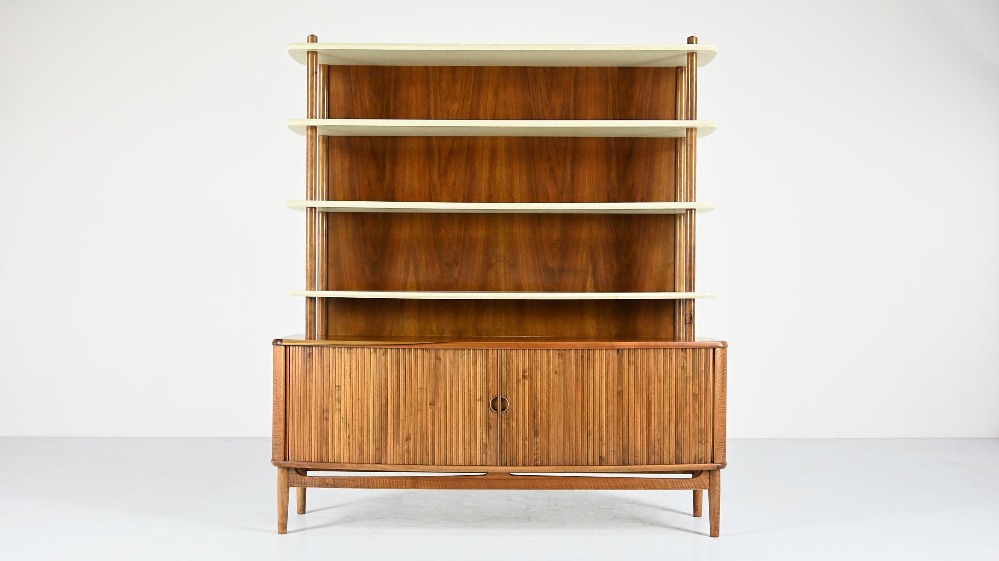Designed by Kurt Olsen for A. Andersen & Bohm, this rare cabinet features a lower section opening by tambour doors revealing shelves and drawers, supporting an upper section of white lacquered shelves. Walnut and walnut veneer, upper shelves in