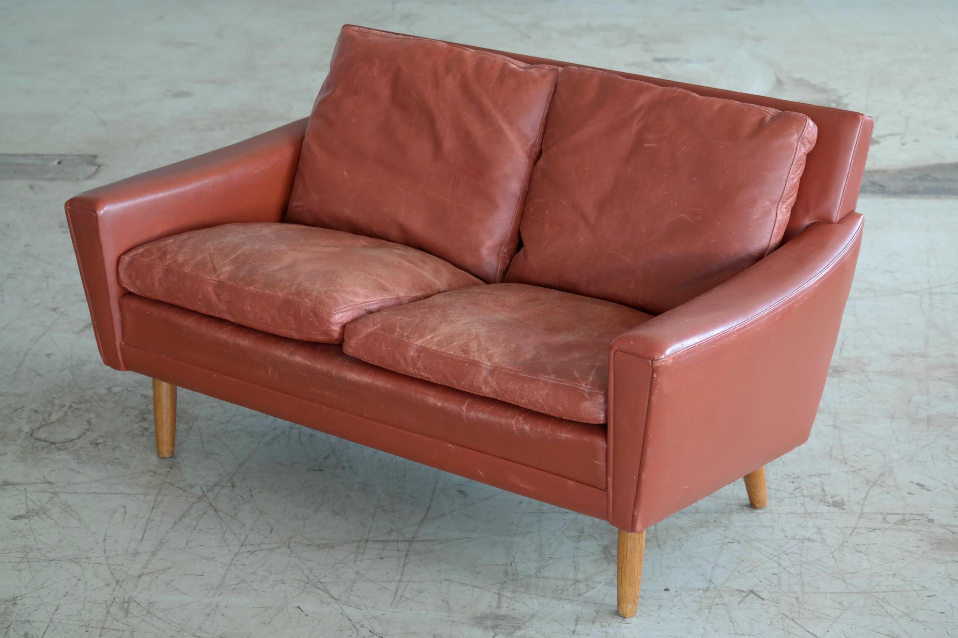 Very elegant Classic midcentury Danish sofa in nice red leather raised on oak legs. Likely made in the 1960s by Rolschau Mobler with the design attributed to Kurt Ostervig. Solid and sturdy and in good vintage condition with the leather still