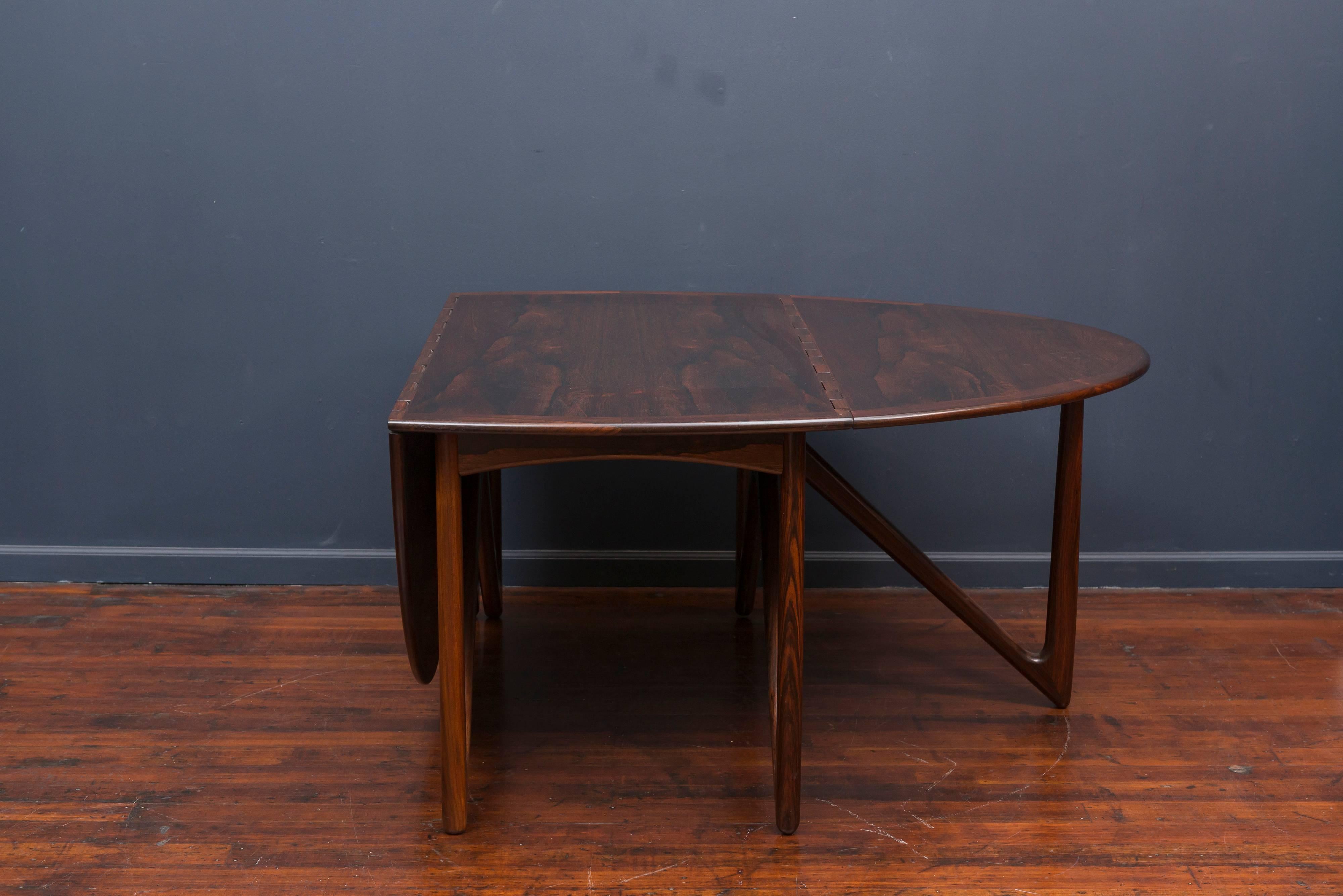 This spectacular rosewood dining table was designed by Niels Koefoed for Koefoeds Hornslet in 1964 (frequently mis-attributed as Kurt Østervig for Jason Møbler) and features an oval top over folding V-legs. The drop leaves move up and down on