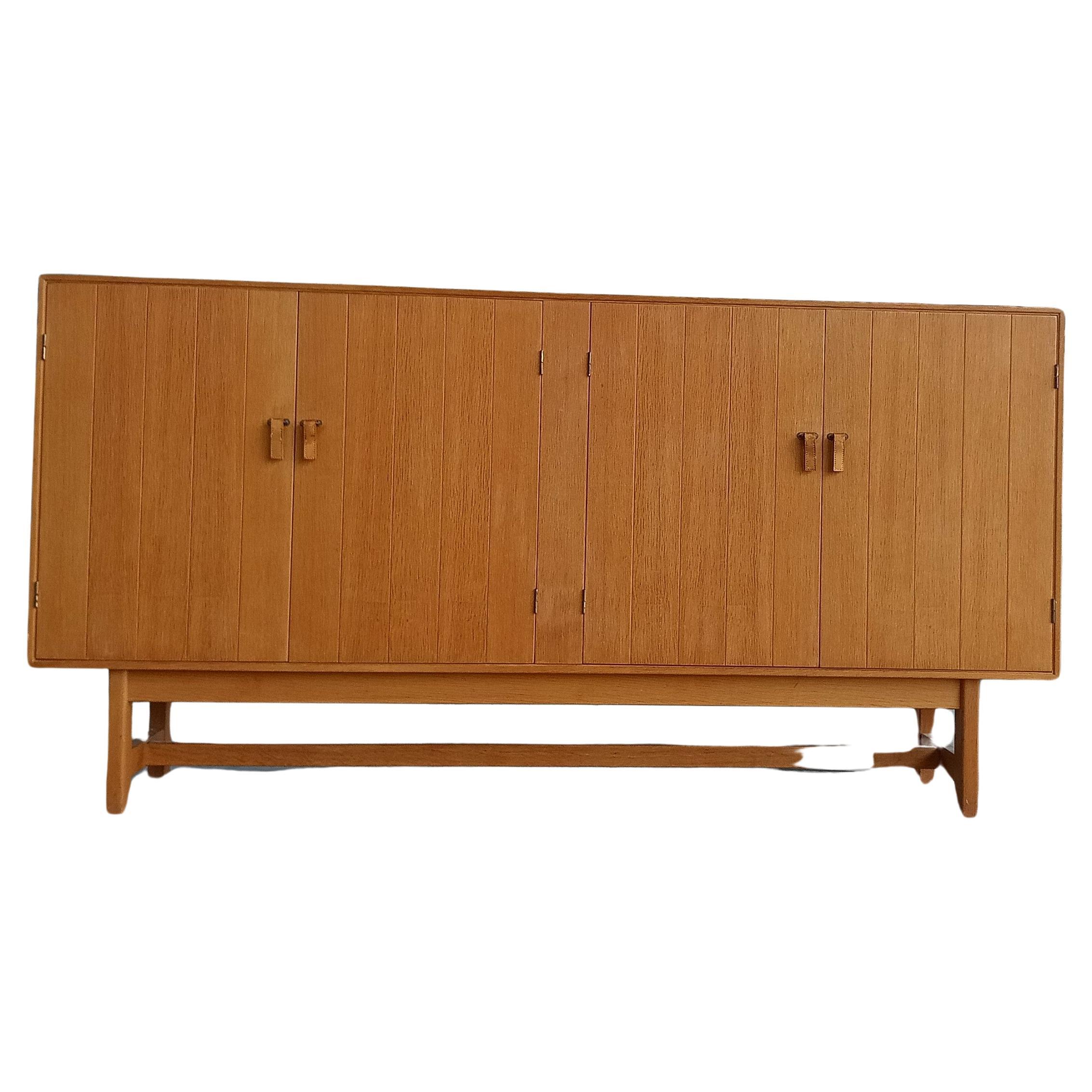 An oak sideboard designed by Kurt Ostervig for KP Mobler, Denmark. 
It has 4 doors with beautiful leather and brass handles.
3 upholstered drawers on the left side.
Besides a slightly visible stain the sideboard is in splendid condition.