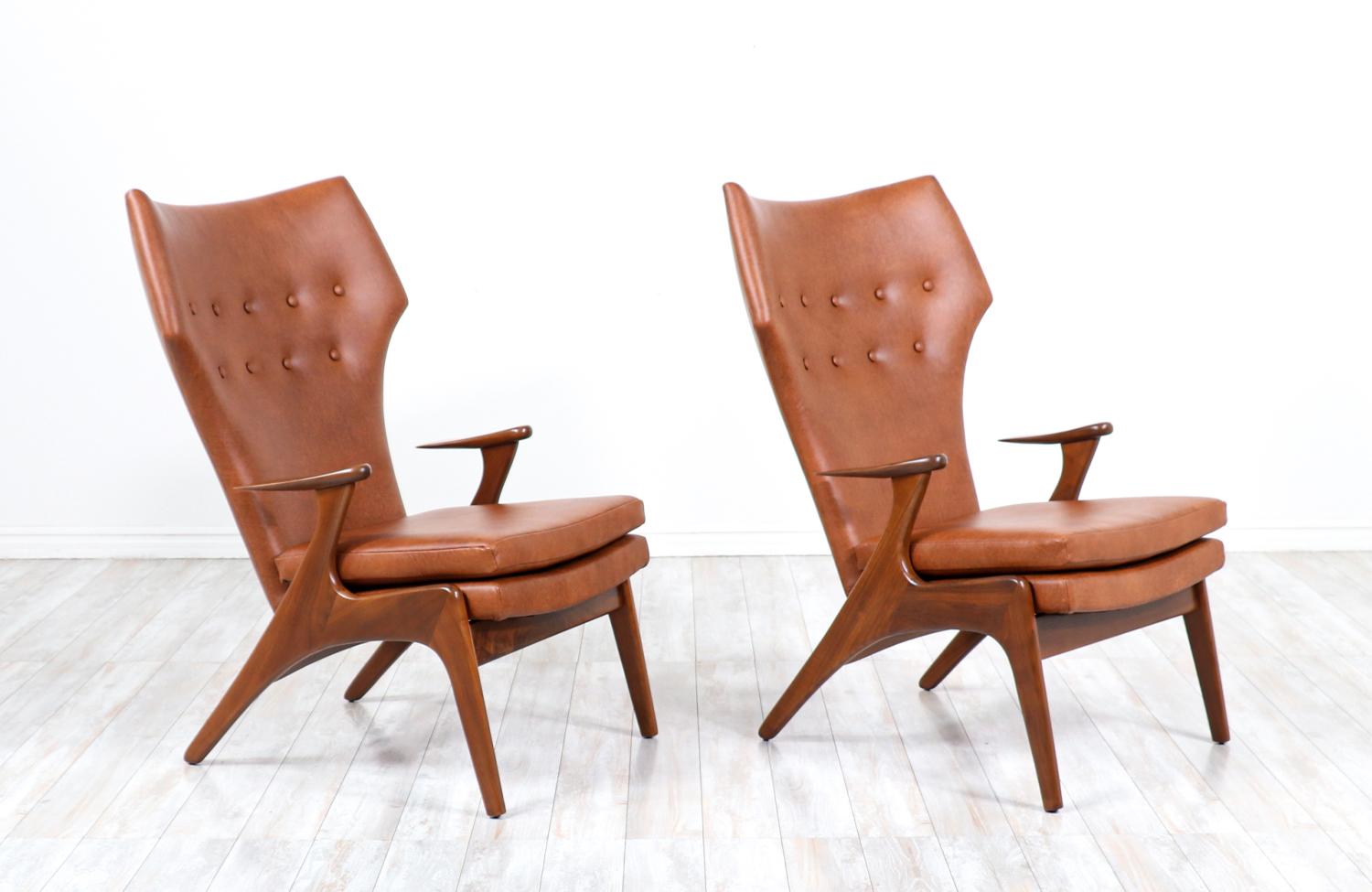 Paire d'élégants fauteuils modernes à haut dossier en forme d'aile, conçus par Kurt Østervig pour Rolschau Møbler au Danemark vers les années 1950. Ces magnifiques chaises sont dotées d'un cadre en bois de noyer massif et d'accoudoirs incurvés en