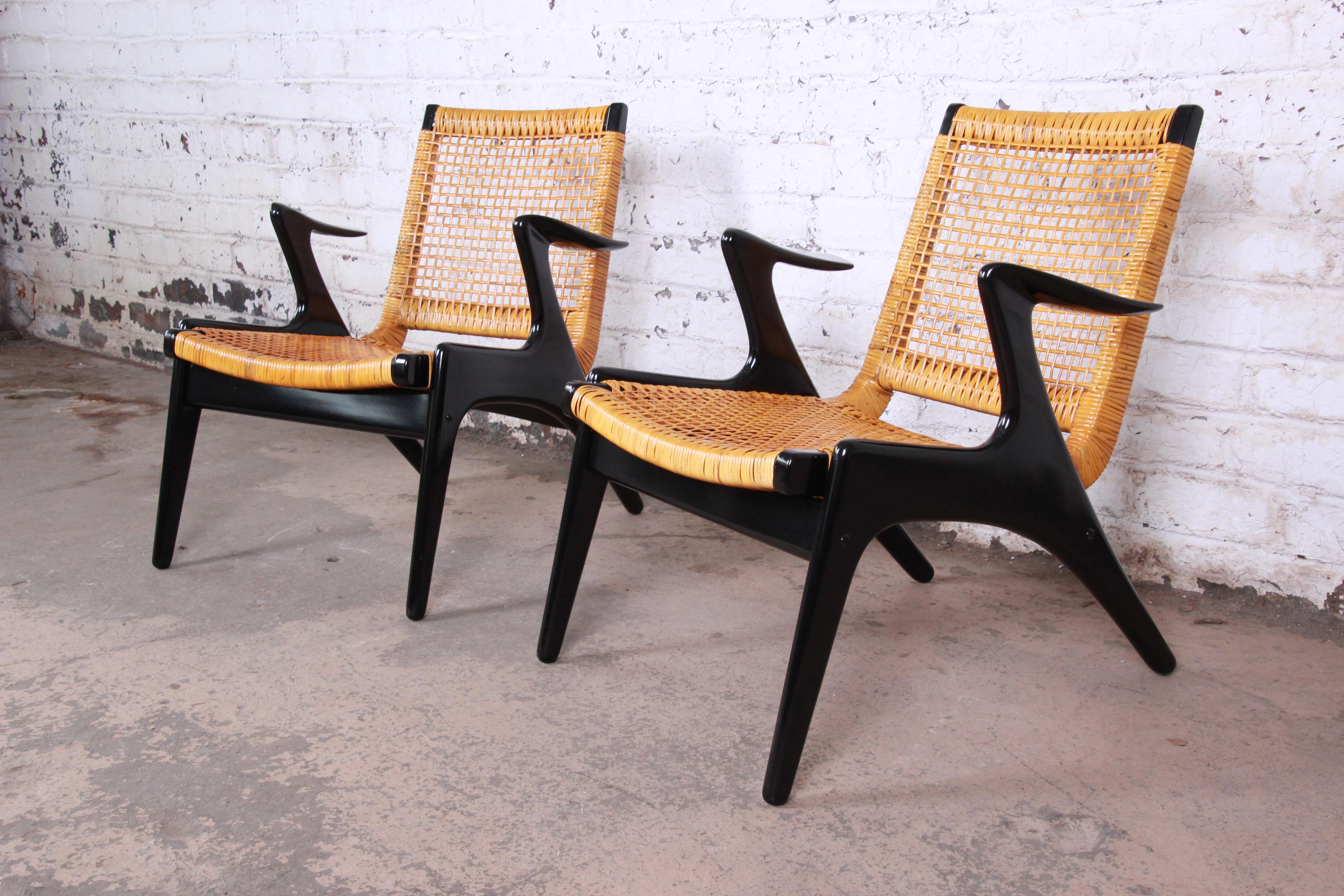 A rare and exceptional pair of mid-century Danish Modern lounge chairs by Kurt Østervig. The chairs feature gorgeous sleek black lacquered frames with unique floating armrests and cane seats and backs. They have been expertly restored and are in