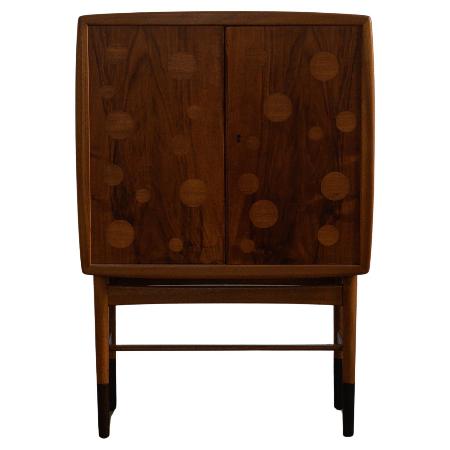 Beautiful and rare 1940 Kurt Østervig Illuminated Cabinet, Model 93 by KP Møbler, Denmark. 

Cabinet features two intarsia designed doors concealing an illuminated interior with three glass shelves above bottle storage, a slide-out table, and two