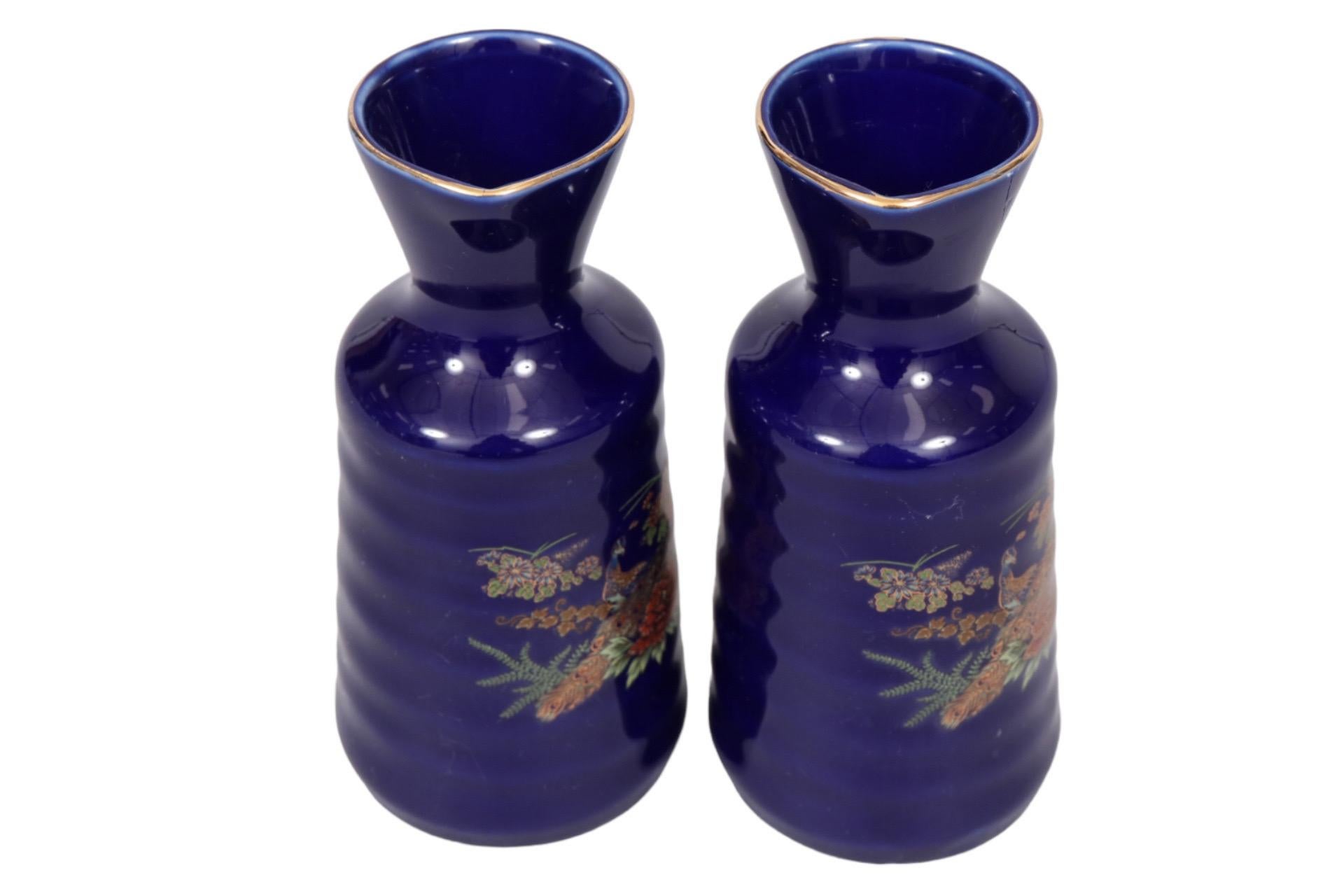 A pair of Kutani hand painted porcelain sake bottles. Cobalt blue rippled bodies are decorated in front with peacocks among red roses. Marked “Kutani” underneath in Kanji, framed in a square. Dimensions per bottle.