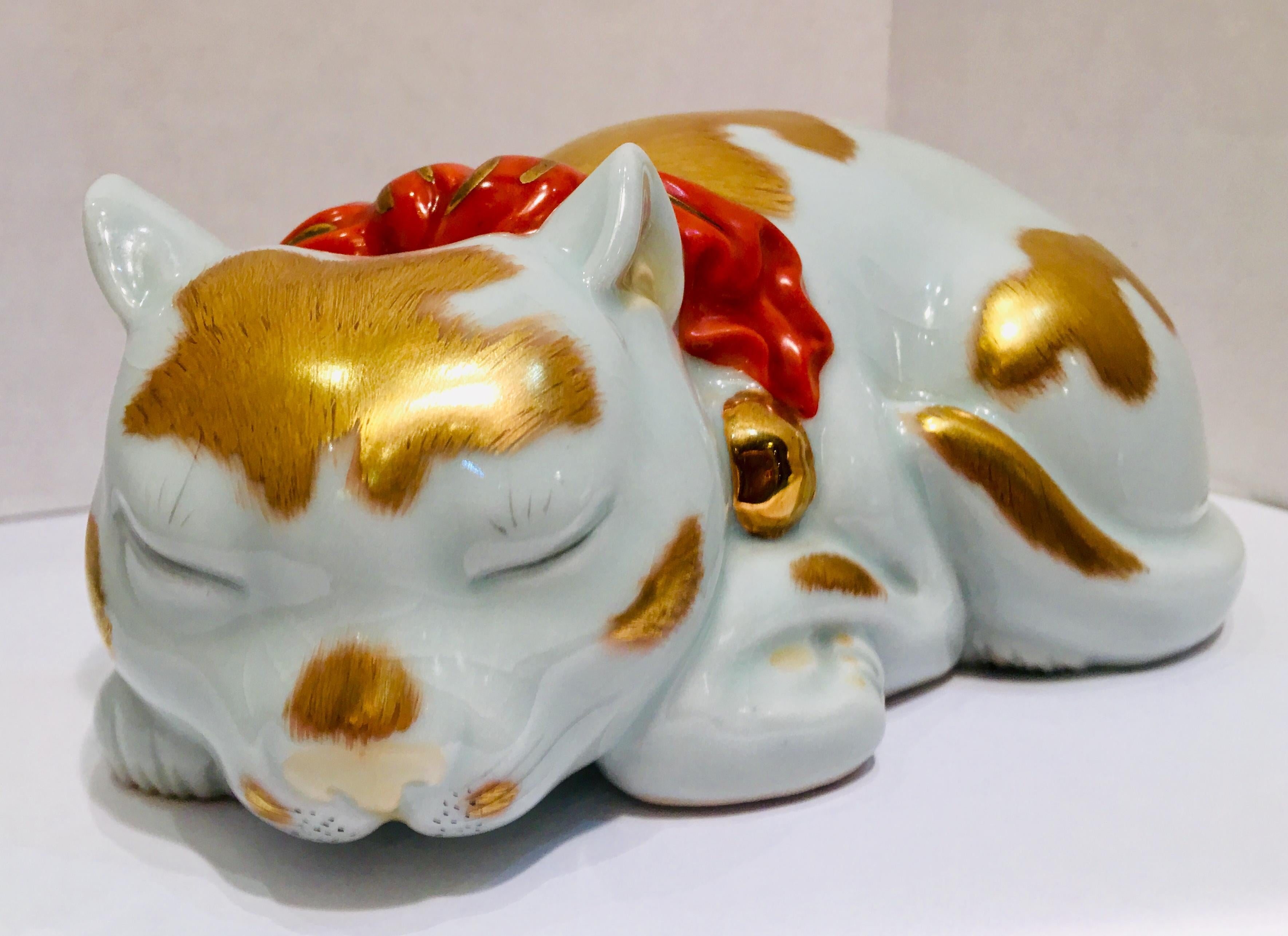 Very precious Kutani Japanese fine porcelain figurine of a curled up, peacefully sleeping small cat or kitten with crackled white glazed finish is lavishly hand painted in 24-karat gold and features a large orange and gold bow with gold
