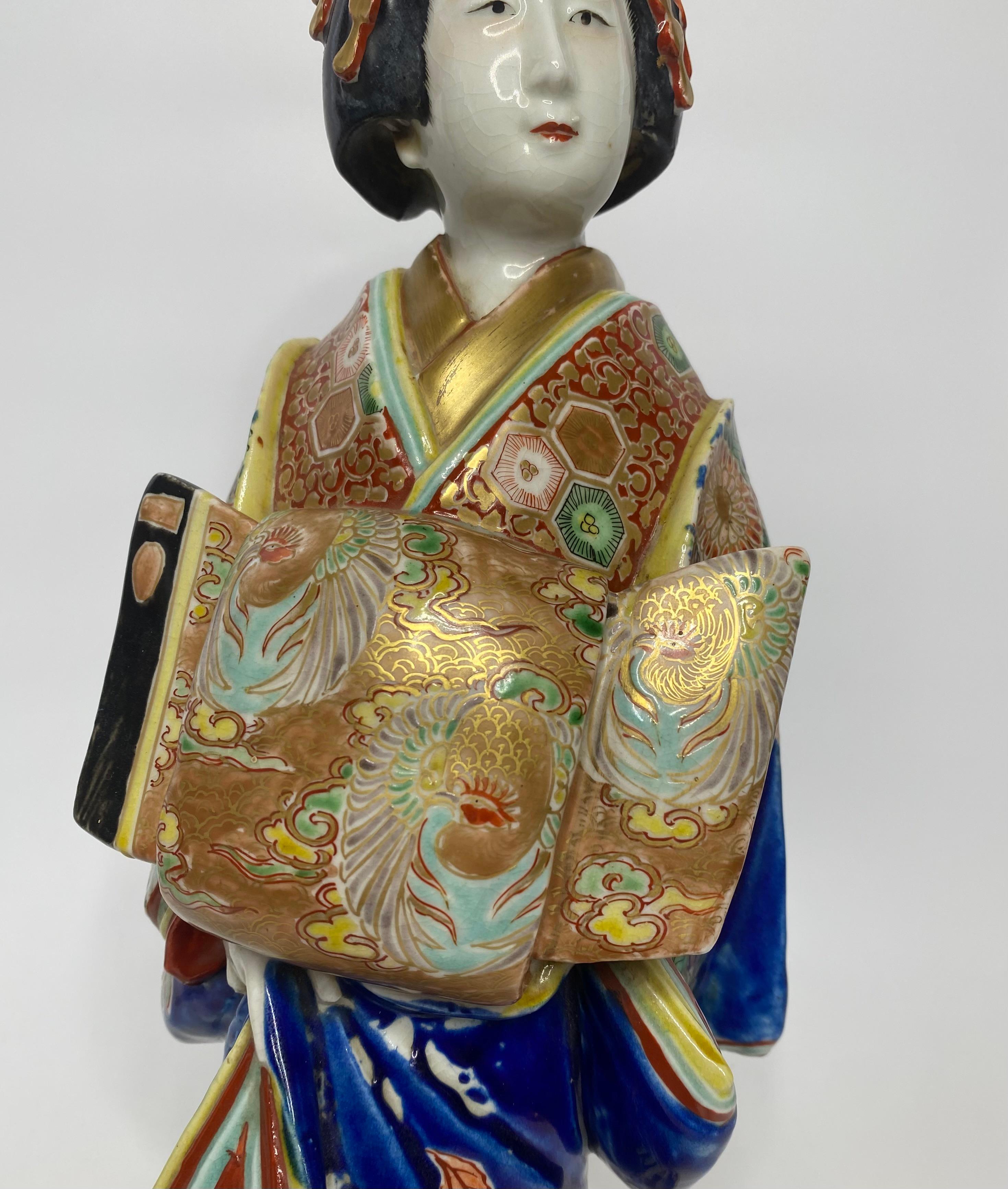 Kutani porcelain Bijin of large size, Japan c. 1900, Meiji Period. The Bijin, wears beautifully decorated traditional costume, the obi particularly well painted with phoenix on a gilt ground.
Her hair held in place with a complex arrangement of