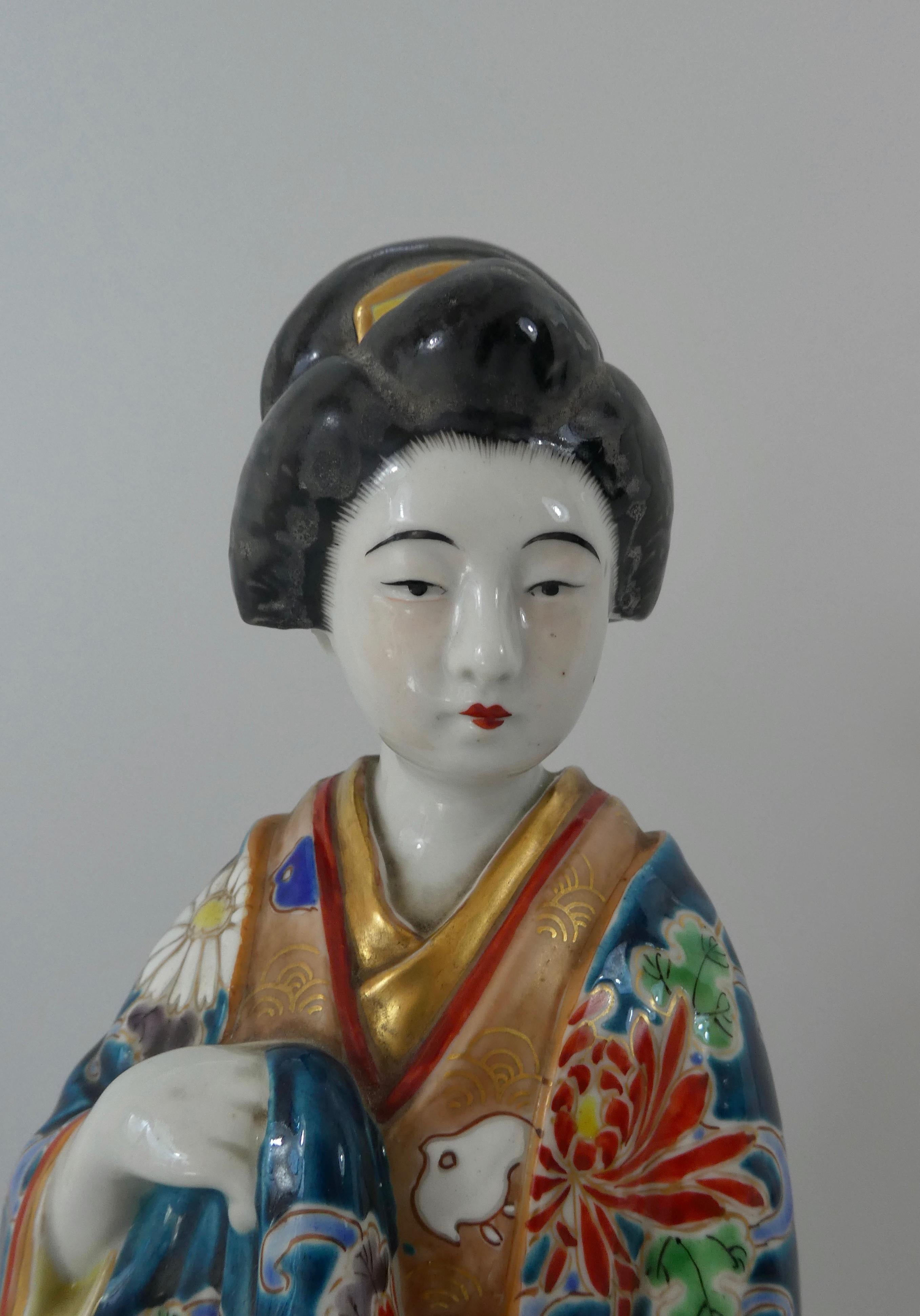 A large Japanese Kutani porcelain figure, Meiji Period (1868-1912). Beautifully modelled as an elegant young girl wearing a blue kimono, decorated in typical enamel, with an image of stylised river strewn with floating flower heads, and birds