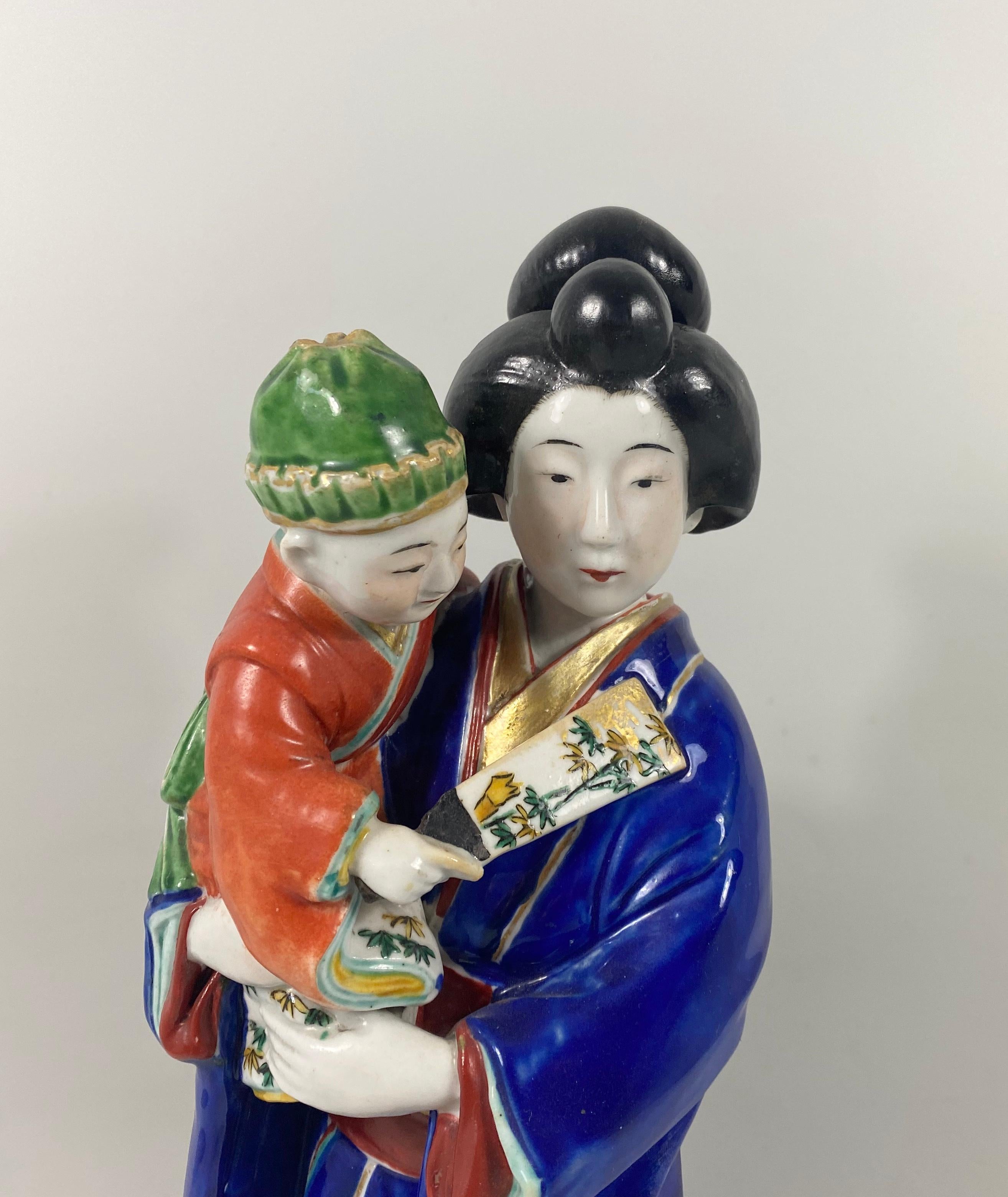 Kutani porcelain figure, Meiji period, (1868-1912). Beautifully modelled as a Bijin, with a young boy. She wears an elaborate kimono, enameled with flowers floating along a river; her red obi, decorated with large flower heads, and gilt karakuso