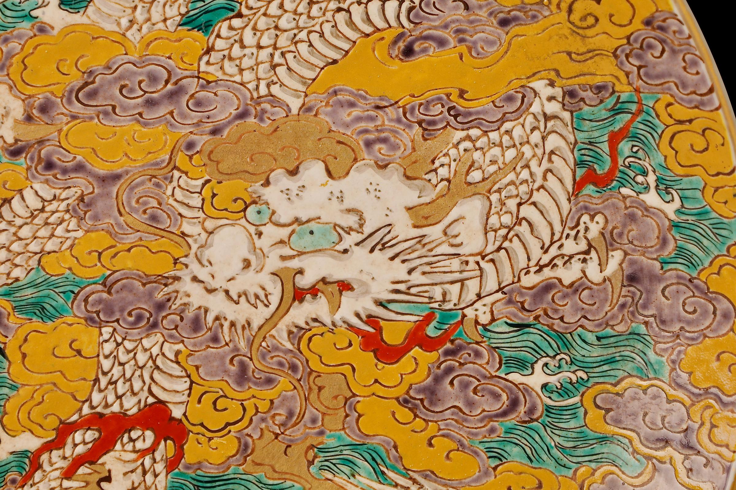 Dieser große Porzellanteller aus Kutani-Ware aus dem 19. Jahrhundert (SKU: ZD66) ist eine Hommage an die japanische Mythologie und die zeitlose Kunst der Porzellanherstellung. Der Teller zeigt eine überschwängliche Drachenszene, die sich inmitten
