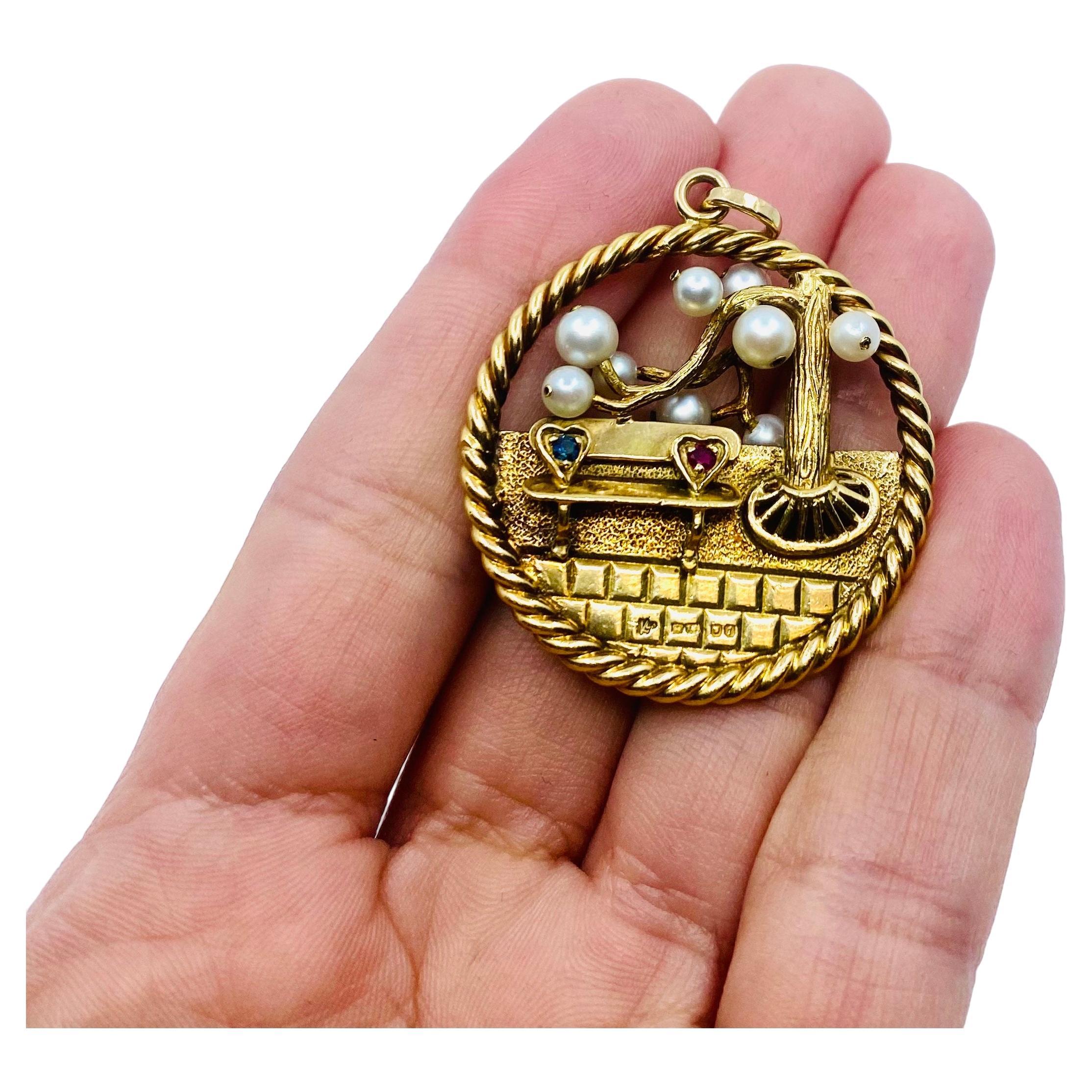 A fun Kutchinsky pendant, made of 18k gold, features sapphires, rubies, and pearls.
The circular pendant is divided in two sections: the top is open work, and the bottom is solid.
The design depicts a stylized tree with the branches decorated with