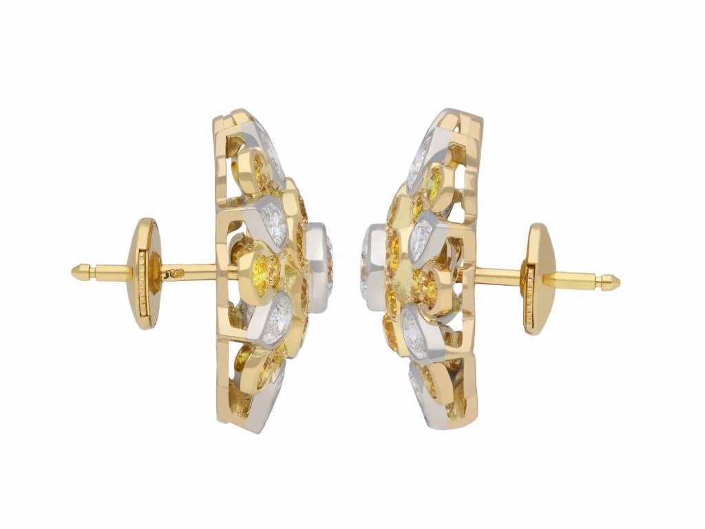 Kutchinsky fancy colour diamond cluster earrings. A matching pair, set to center with a round brilliant cut diamond in an open back rubover setting, two in total with a combined approximate weight of 0.80 carats, encircled by twenty four round