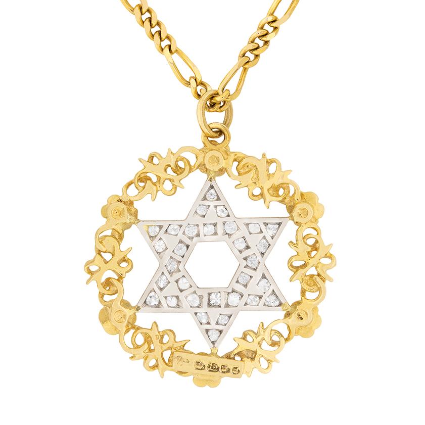 Dating to the 1950s, this Star of David pendant is made in 18 carat yellow gold and 18 carat white gold. The star is grain set with round brilliant diamonds totalling 0.90 carat. They are estimated as F in colour and VS in clarity. The halo