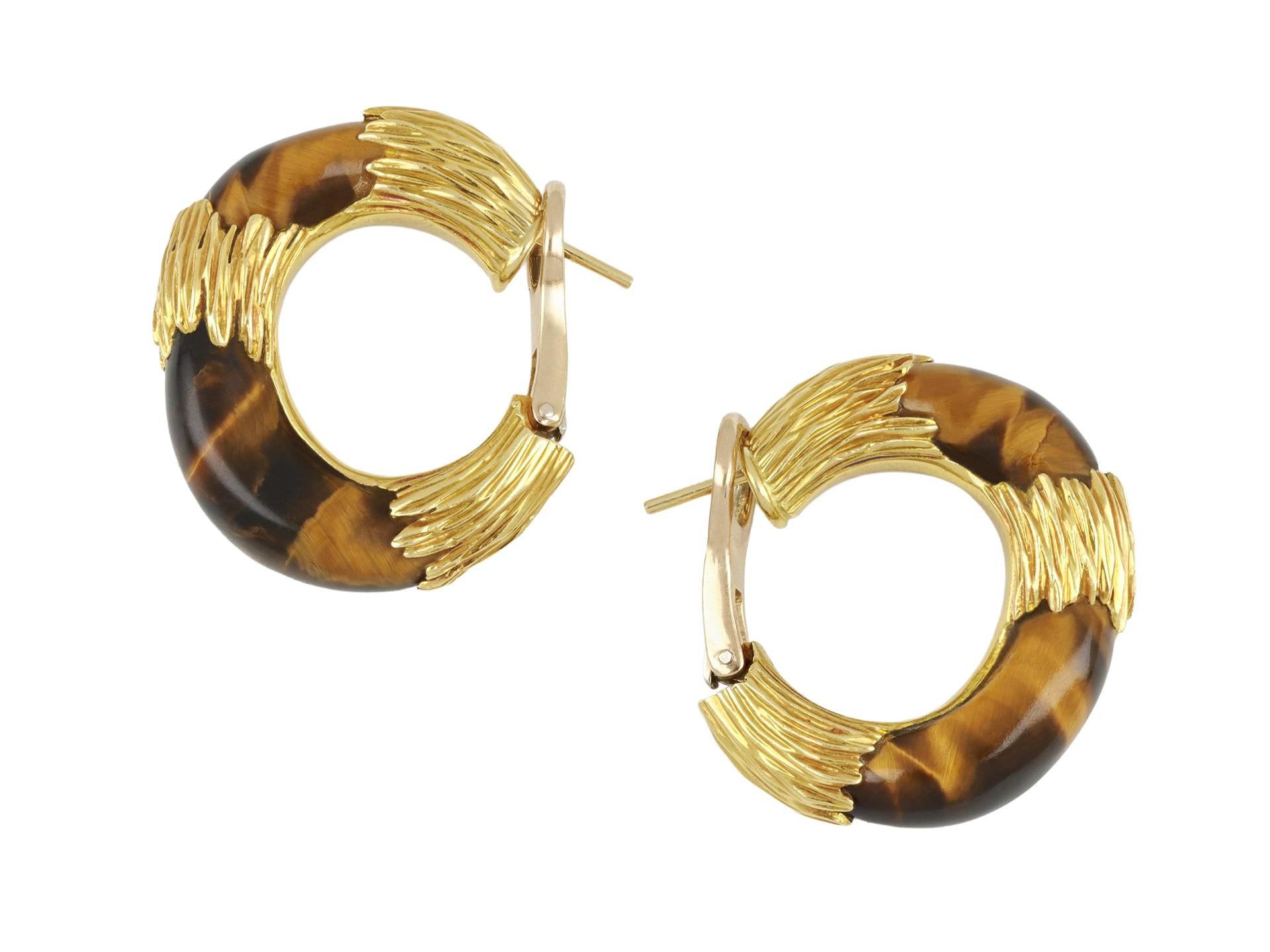 Boucles d'oreilles en œil de tigre de Kutchinsky. Une paire assortie, chacune sertie d'un œil de tigre sculpté, à un anneau audacieux présentant des détails en or texturé, muni au verso d'une tige sécurisée et d'un clip à charnière, d'une longueur