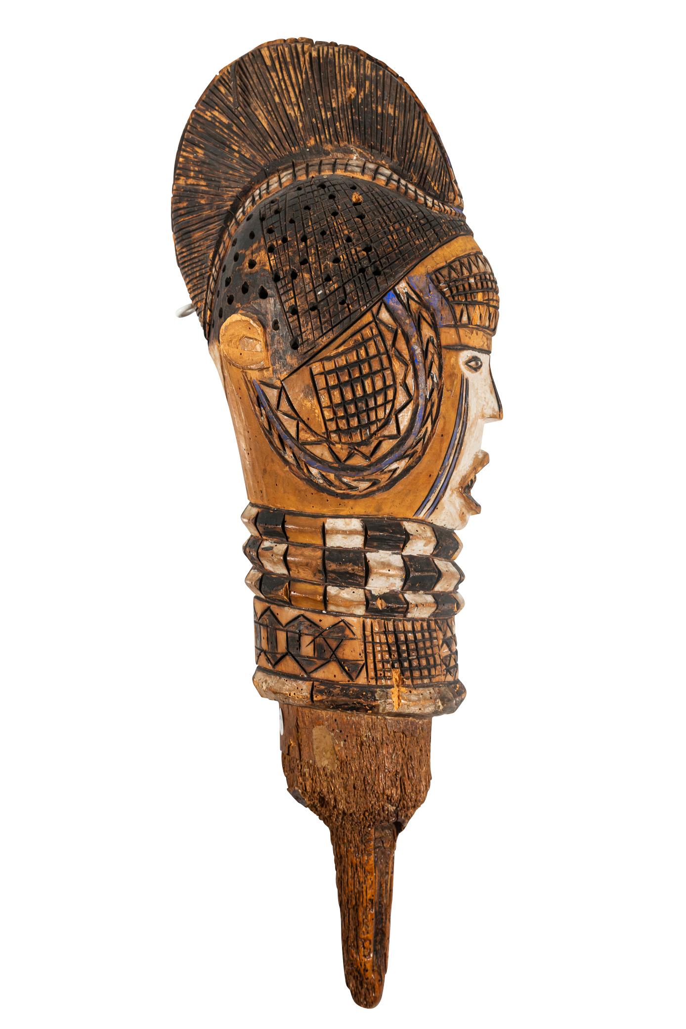 Kuyu puppet head, 
Wood and white, black and blue pigments,
The cylindrical handle supporting a rounded head with almond-shaped eyes, the half-open mouth revealing a row of teeth, the neck with rows of geometric patterns, the bun hairstyle, the face