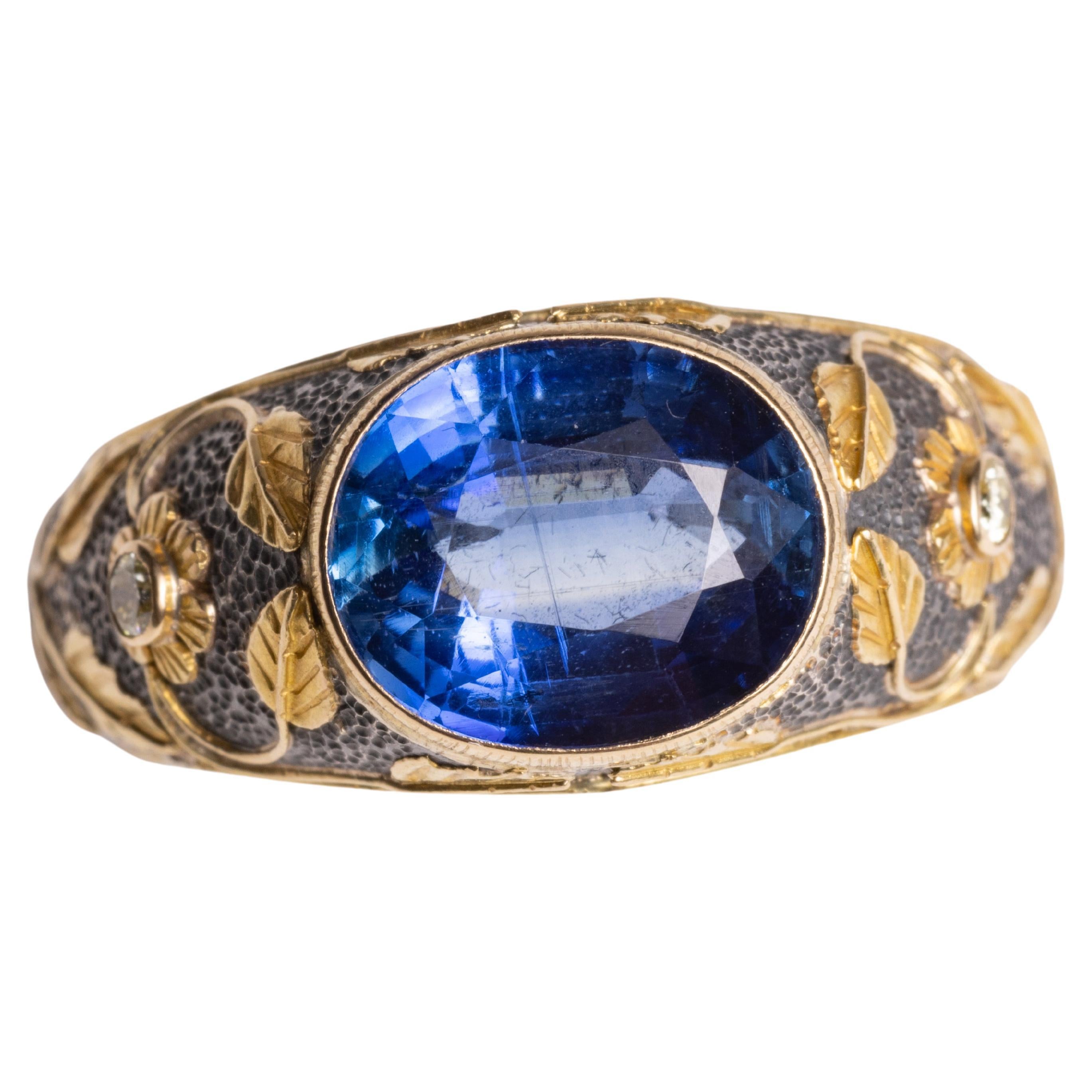 A stunning faceted, oval blue kyanite center gemstone in a sterling silver ring with 18K gold overlay in a floral and vine motif.  Two round diamonds create the center of the two flowers on the sides.  Ring size is an 8.

The fine jewelry collection