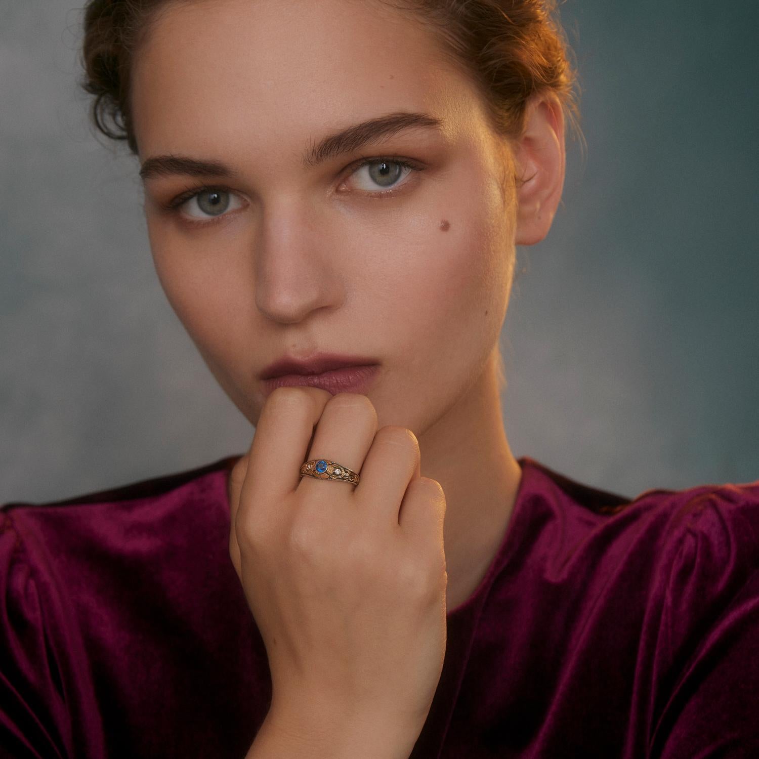 Cette jolie bague en kyanite et diamant est unique en son genre. Elle comporte une pierre précieuse centrale en kyanite, flanquée de deux diamants pleine taille, le tout serti dans des motifs de fleurs et de feuilles gravés à la main en or jaune 18
