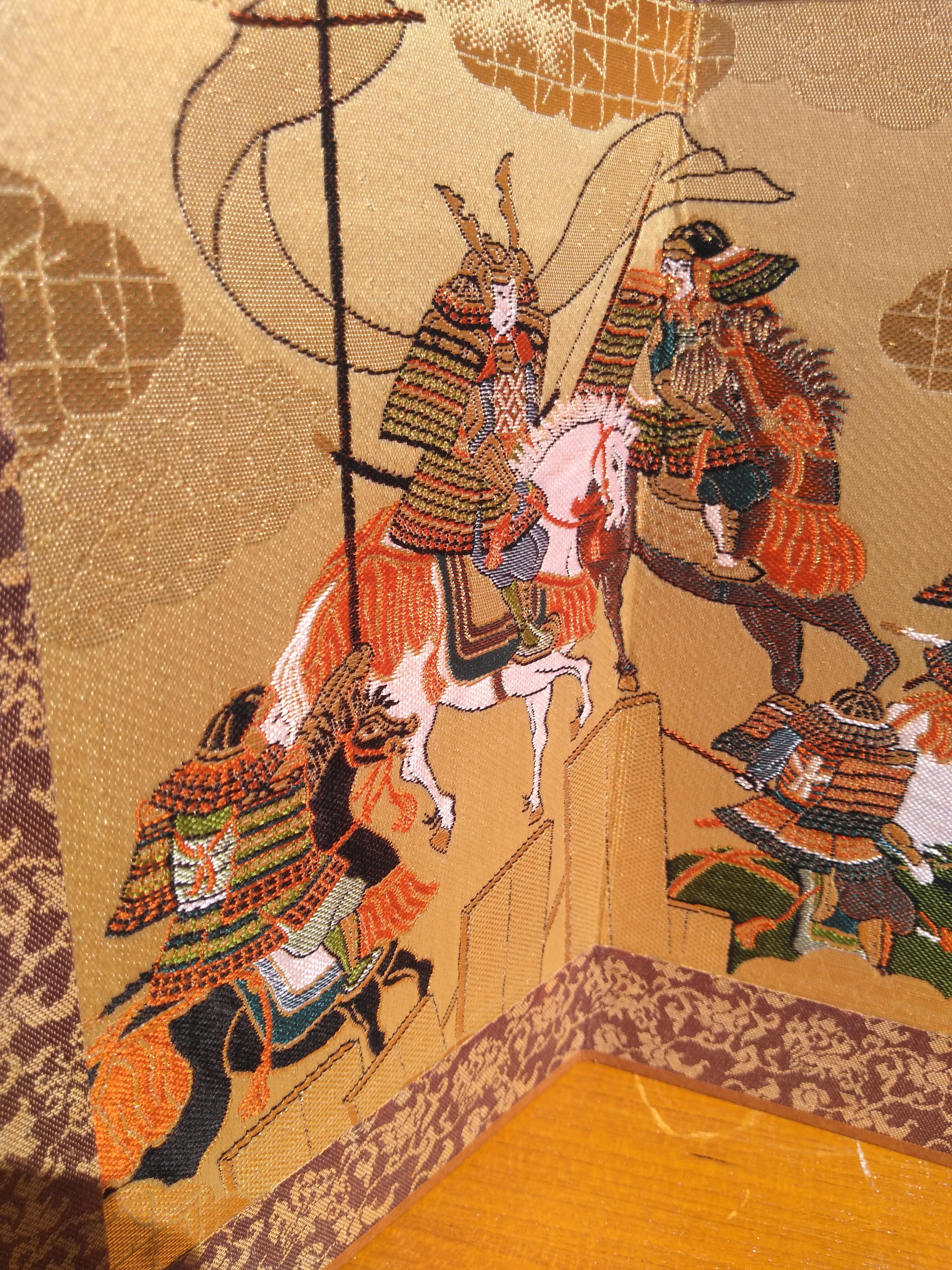 Dieser Kyonoshiki Foldes Paravent ist handgewebt. Es ist im traditionellen Stil der berühmten Webstühle von Kyoto, Japan, gefertigt. Es ist mit Gold- und Silberfäden auf Seide gestickt. Es zeigt die Samurai in einer dem Kubuki-Theater ähnlichen