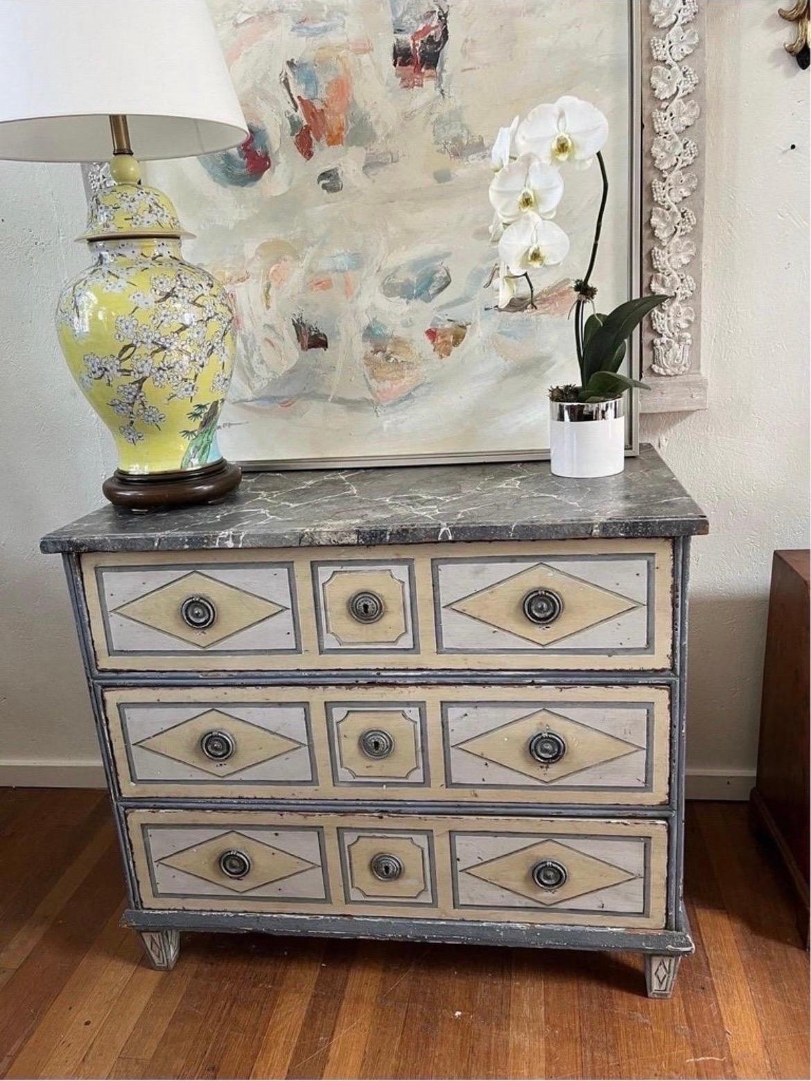 French, late 18th century.

A French late 18th century three drawer chest or commode having geometric painted panels to the drawers and sides. Each drawer has two ring pulls and a central key hole. The top has a faux marbleized finish and verso with