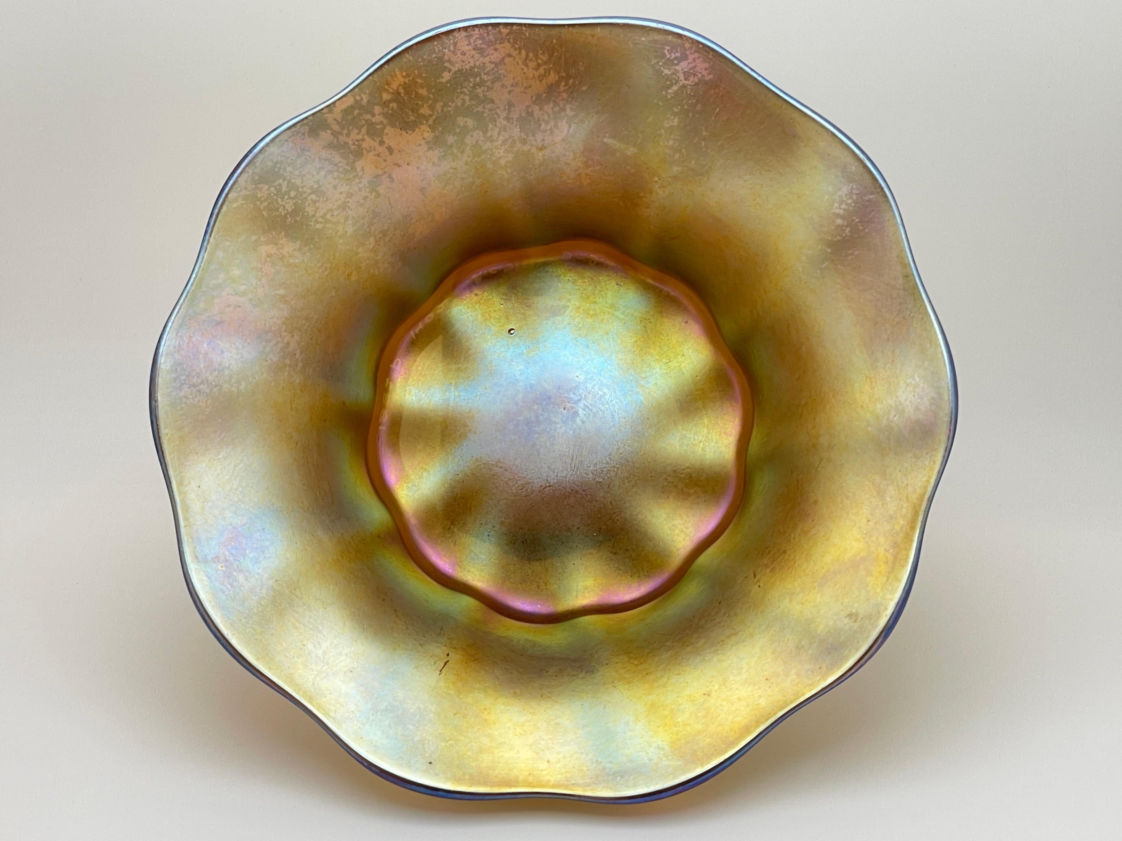This exquisite Louis Comfort Tiffany Favrile glass bowl is a true masterpiece of American Art Nouveau craftsmanship, Circa 1882. This rare and elegant piece shimmers with a stunning iridescent gold hue, enhanced by delicate undertones of pink, blue,