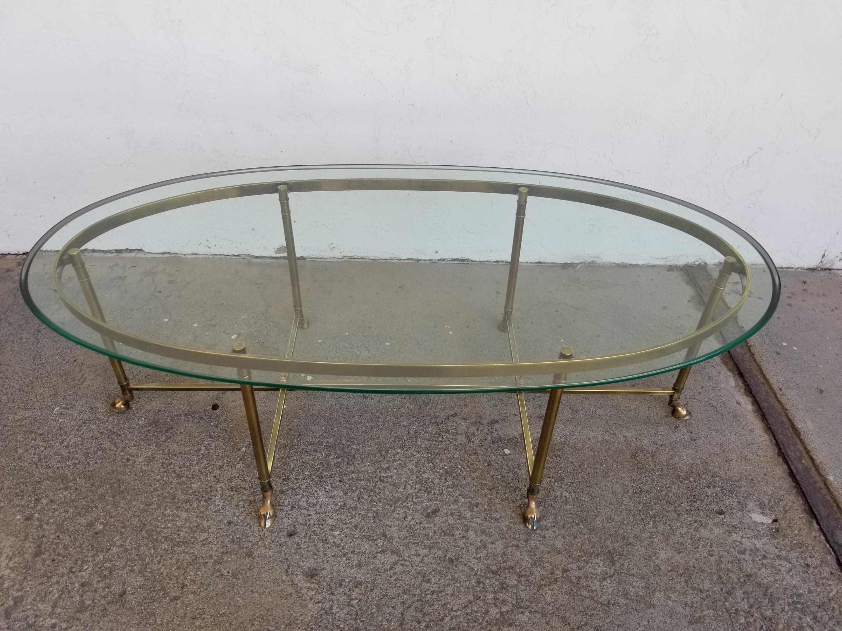Fine and elegant solid brass coffee table with amazing beveled glass oval top. Hoof feet detail. Very good original vintage condition with original glass top.