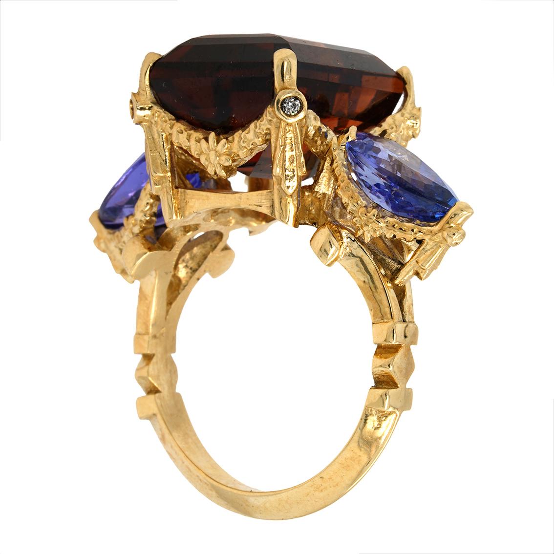 Exquisitely handcrafted in 9kt yellow gold this stunning ring features a decadent rich cognac colored emerald cut tourmaline aloft a signature William Llewellyn Griffiths garland setting studded with four 1.4mm round brilliant cut white (E/F,VVs)