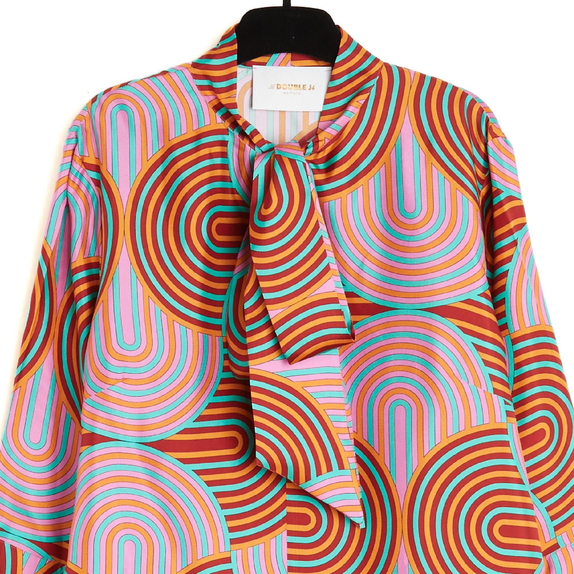 Blusa La Double J 2017 de sarga de seda con estampado geométrico en tonos rosa, naranja, rojo y verde. Corte recto, redondo, escote con abertura en forma de lágrima con un largo lazo de lavallière, mangas largas acabadas con un amplio volante atado