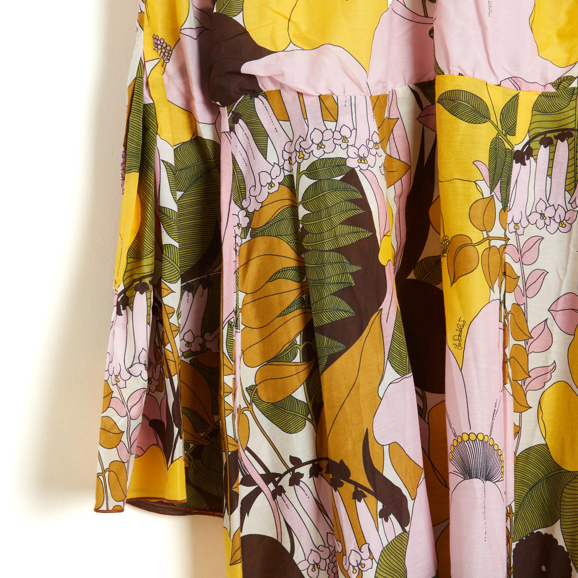 Robe longue La Double J, collection 2023 en popeline de coton et soie blanche imprimée d'un large motif floral rose pâle, jaune, kaki et marron, col rond froncé par un lien et fermé par 7 boutons de robe jusqu'à la taille, légèrement resserrée, jupe