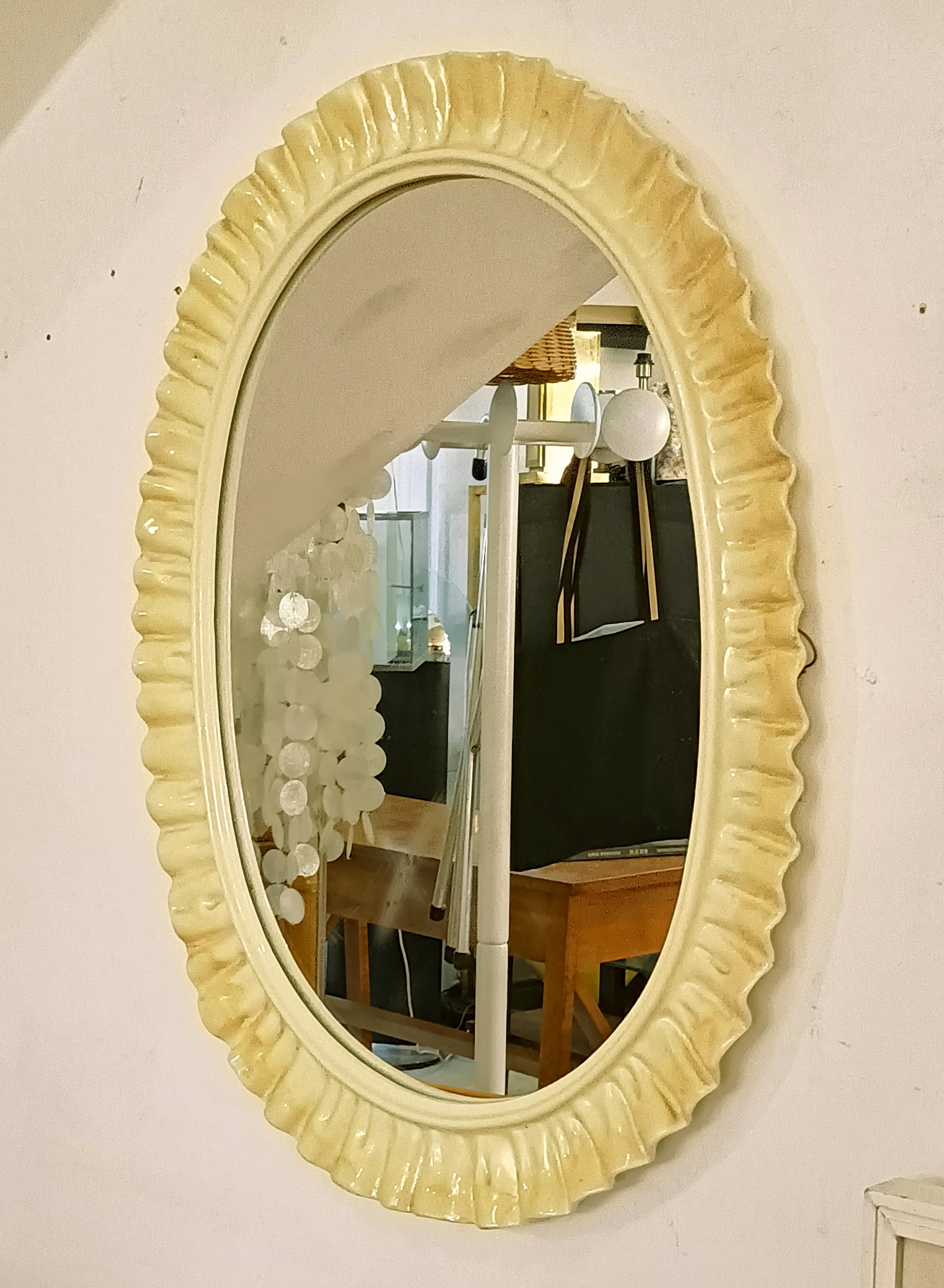 Raro specchio da parete ovale con cornice in ceramica smaltata nei toni del giallo e cristallo specchiato, marchio originale del produttore sul bordo La Farnesiana Parma Made in Italy 1958