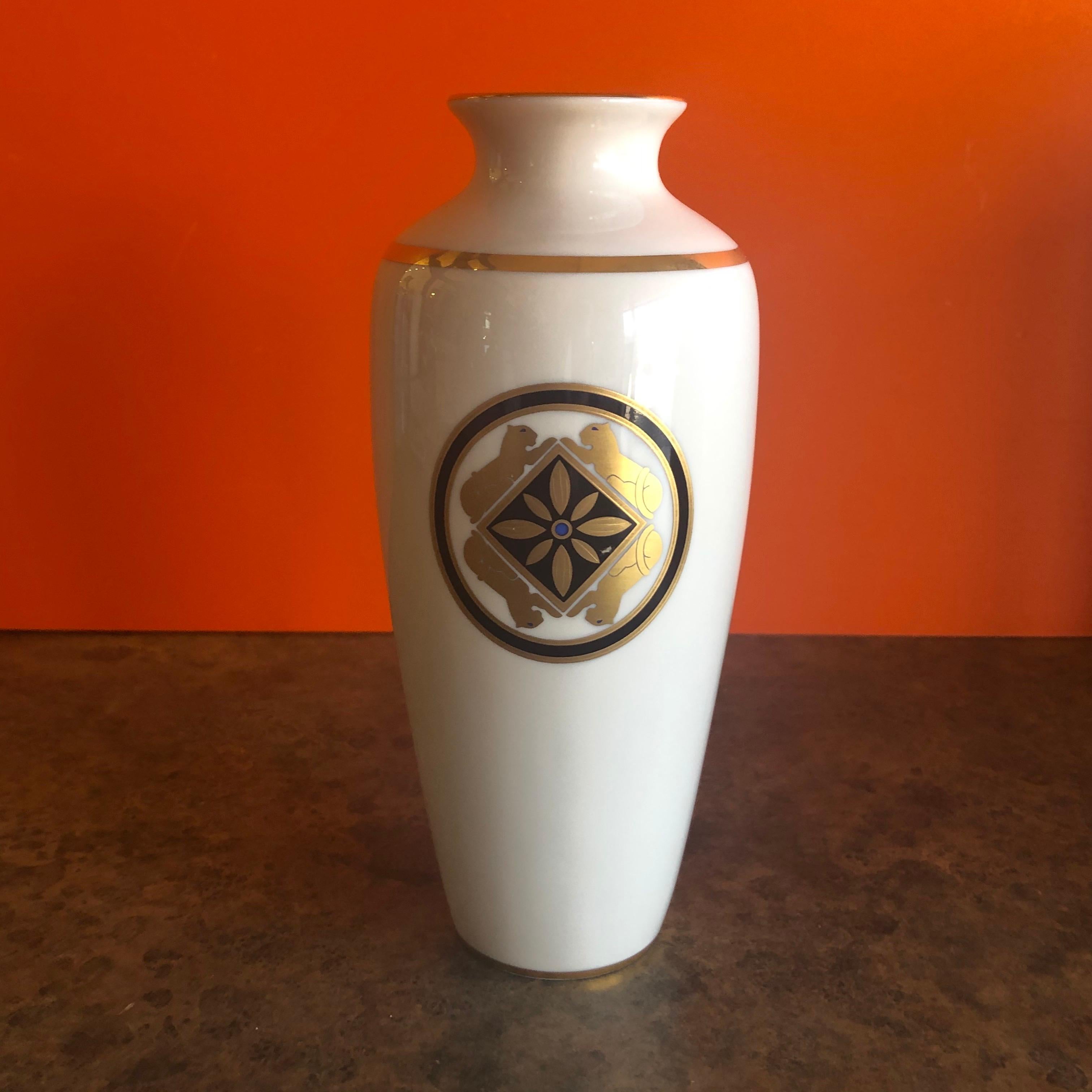 La Maison de L' Art Deco porcelain vase by Cartier, circa 1986. The vase features a gilded rim, funnel shaped neck, and tapered cylindrical body. The exterior features a band of gilt work at the shoulder and base, and a pair of medallions with a