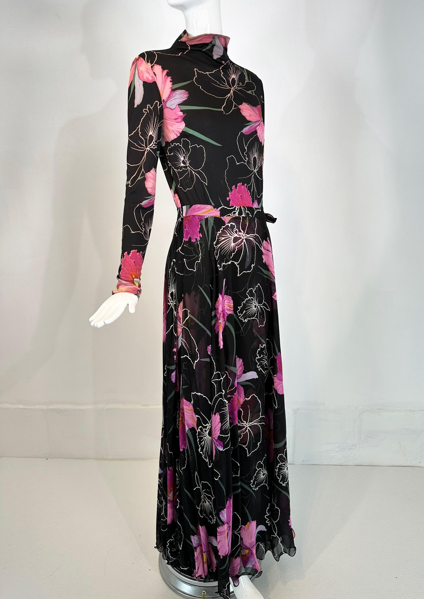 La Mendola 2pc orchid print jersey maxi dress & silk chiffon over skirt from the 1960s. Floral print of large orchid flowers with white outline orchid flowers on a black ground. Mock neck dress has long sleeves, the dress has bust darts. Body