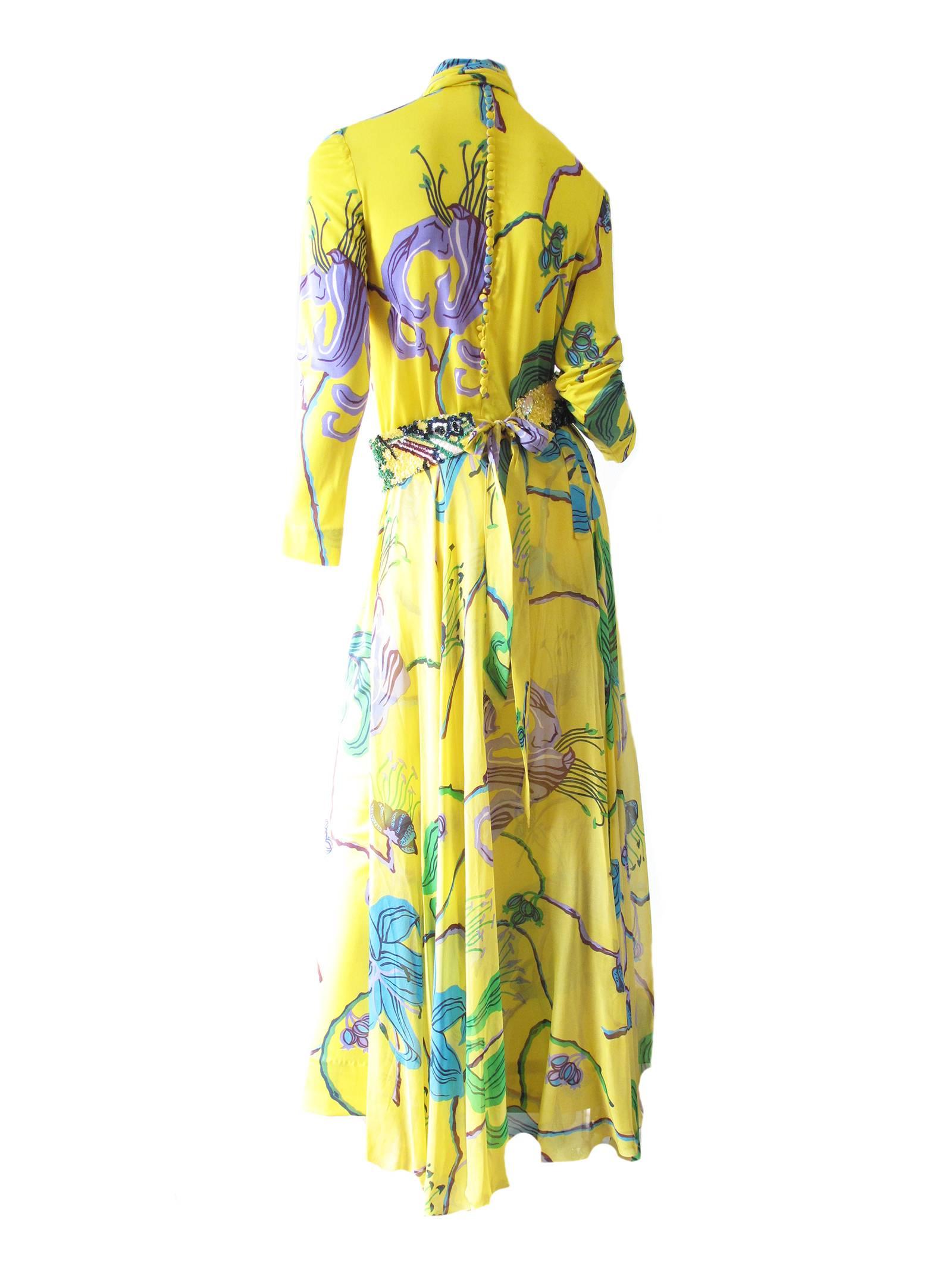 La Mendola Printed Gown with Over Skirt and Sequin Belt.  Floral pattern on yellow background in synthetic jersey. With a silk chiffon over skirt. The dress closes in the back with 40 small covered buttons.  Comes with sequin tie belt and fabric tie