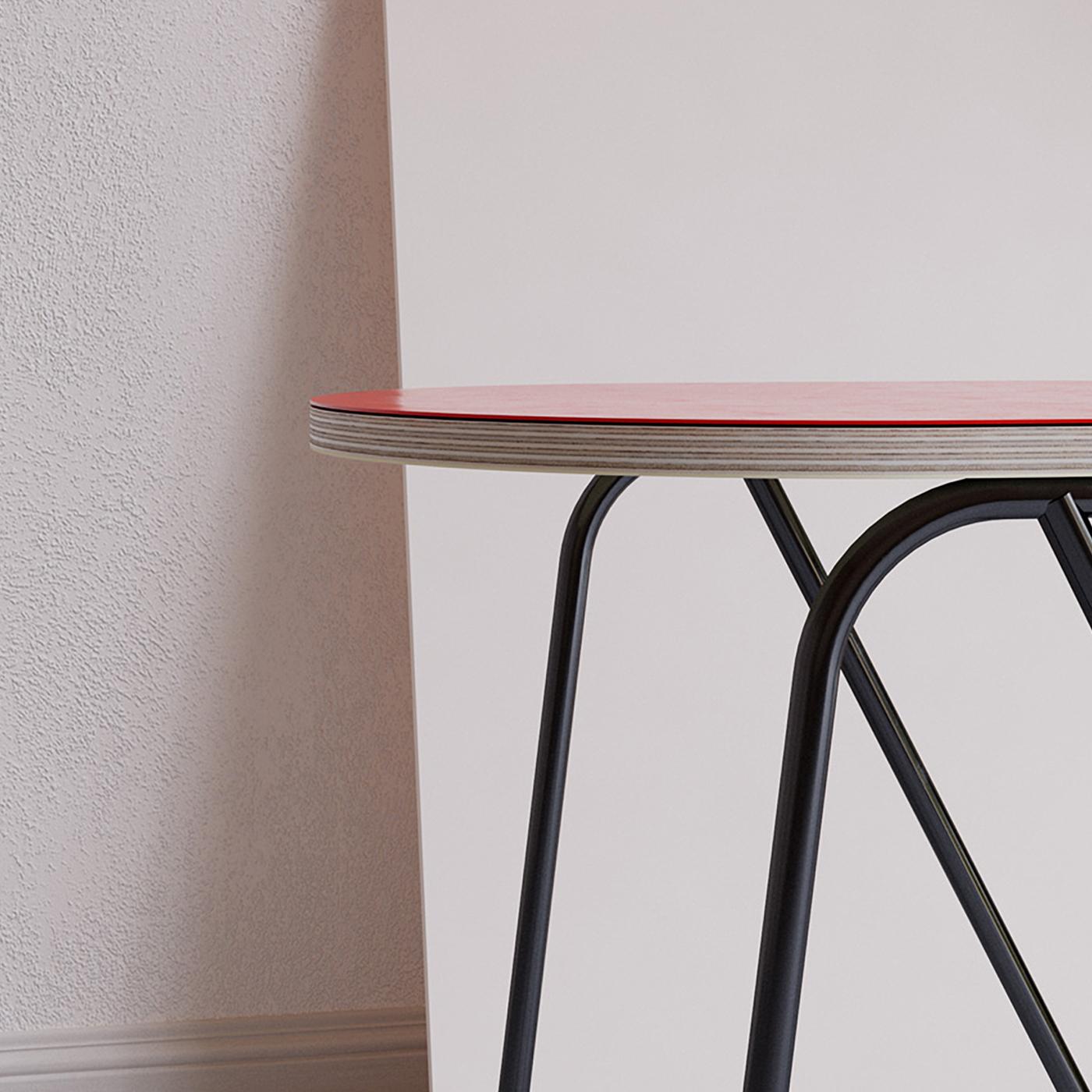 A quiet asymmetrical twist distinguishes this round side table from the La Misciù Collection. The wooden top finished in red rests on an airy cylindrical steel base comprised of two front legs and of a U-shaped element offering efficient rear