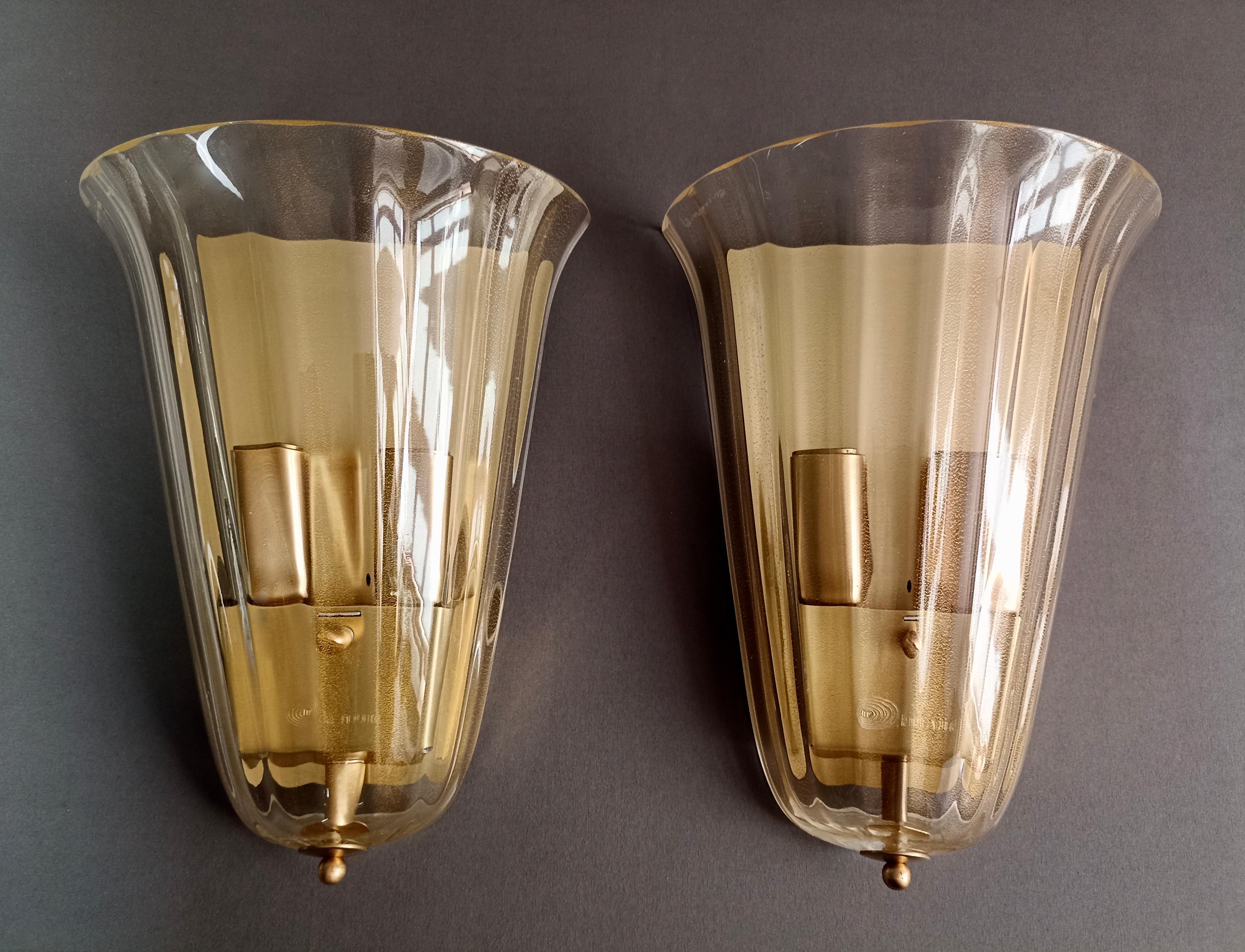 Satz von zwei wunderschönen zweiflammigen La Murrina-Leuchten aus den 1990er Jahren aus klarem Muranoglas mit goldenen Einschlüssen und wunderschöner gerippter Verarbeitung. Großer Stil.
Die Sockel und Lampenabdeckungen sind aus vergoldetem