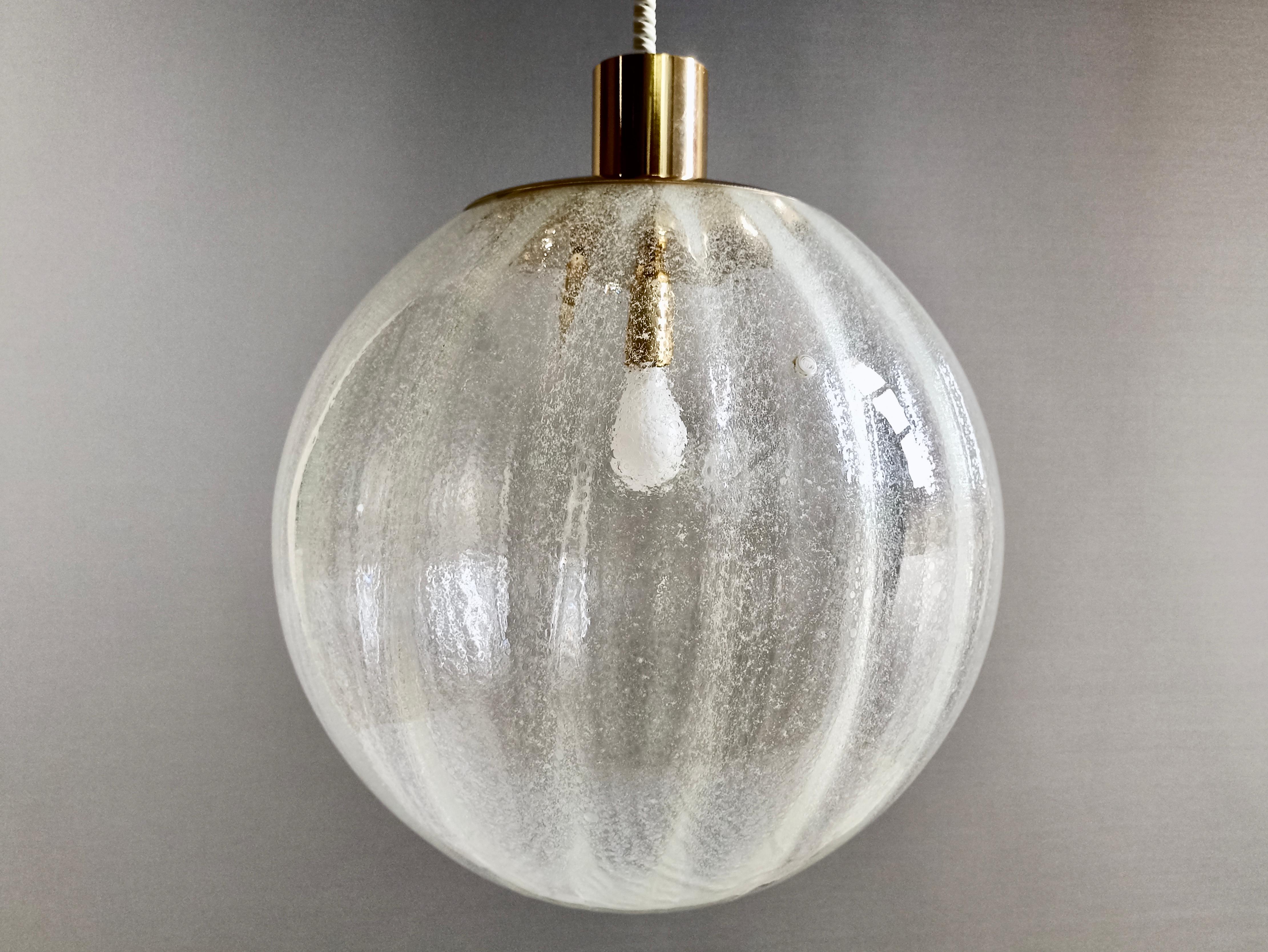 La Murrina 1970s large pendant lamp in Murano 'Pulegoso' art glass and gilded brass frame. The lamp is fixed to the ceiling with a steel wire and has a slightly downward pointing shape.
The surface of the clear glass sphere is as if wrapped in a