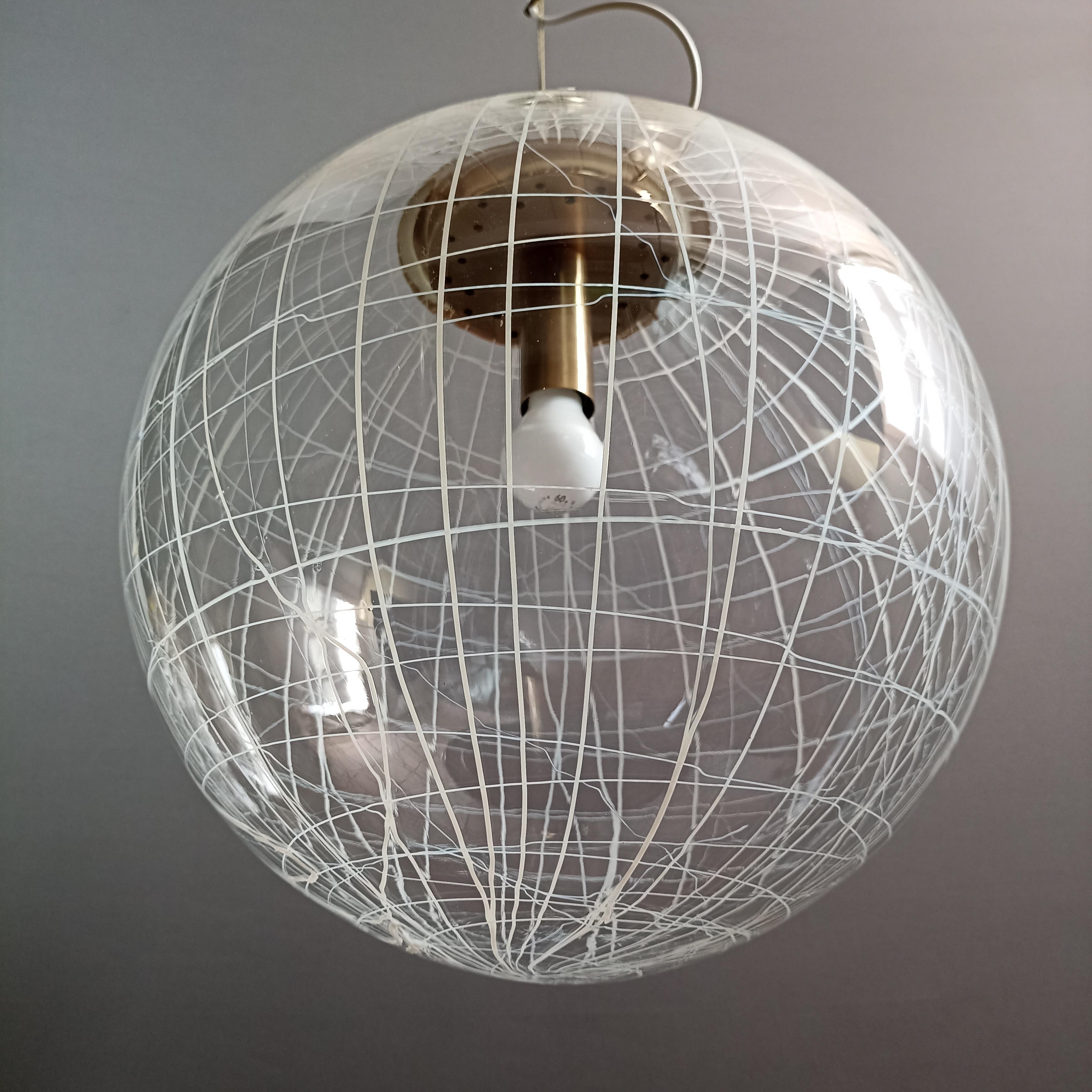 La Murrina large single-light Space Age pendant lamp from the 1970s in Murano art glass and metal frame with a brushed brass finish. The lamp is fixed to the ceiling with a double steel wire.
The surface of the transparent glass sphere appears as