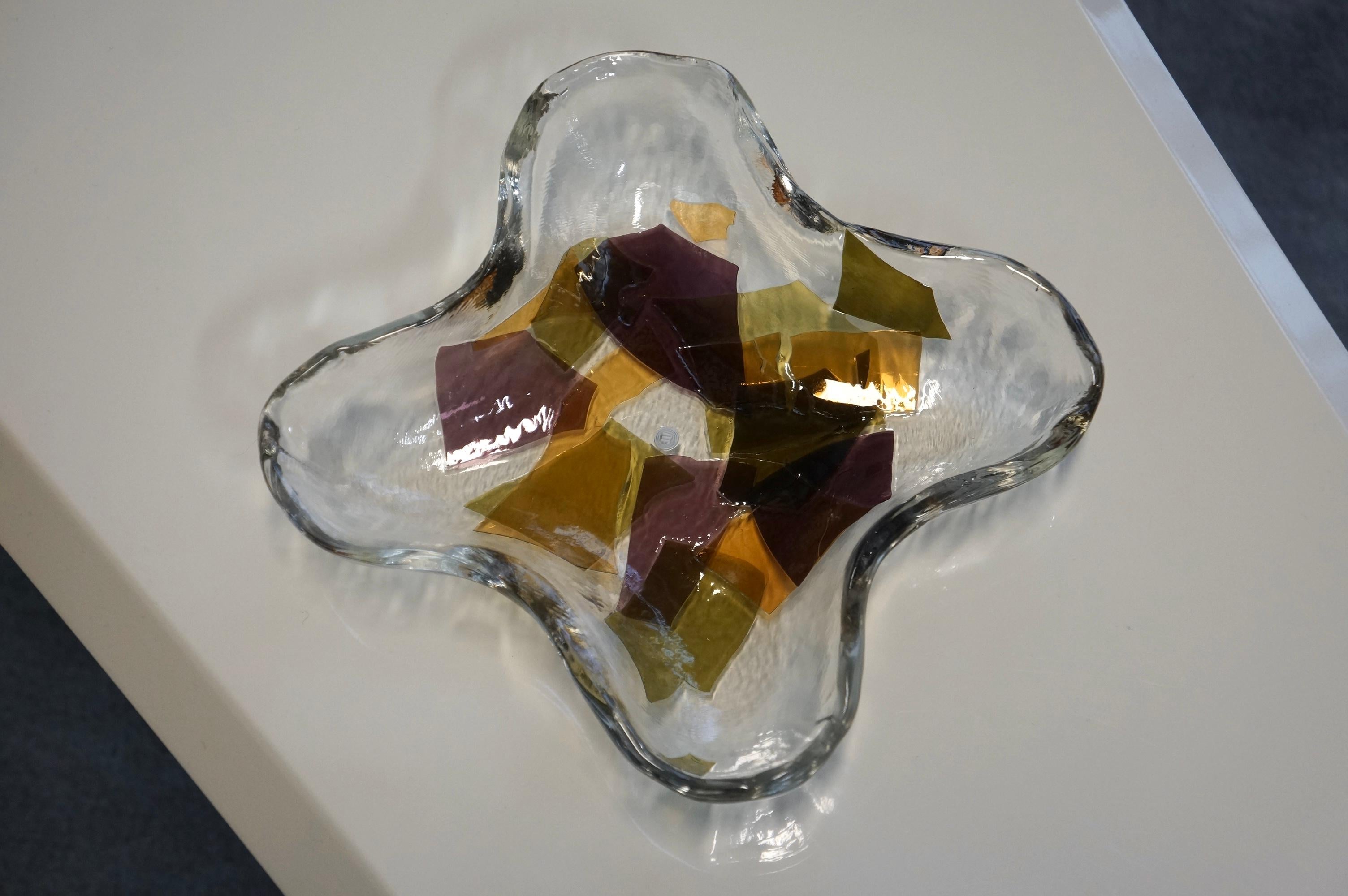Stunning original ‘La Murrina’ decorative Murano Art glass dish featuring coloured glass. The clear art glass has a pinched and symmetrical shape. It is enriched with thin layers of coloured art glass fragments varying from yellow to purple. The