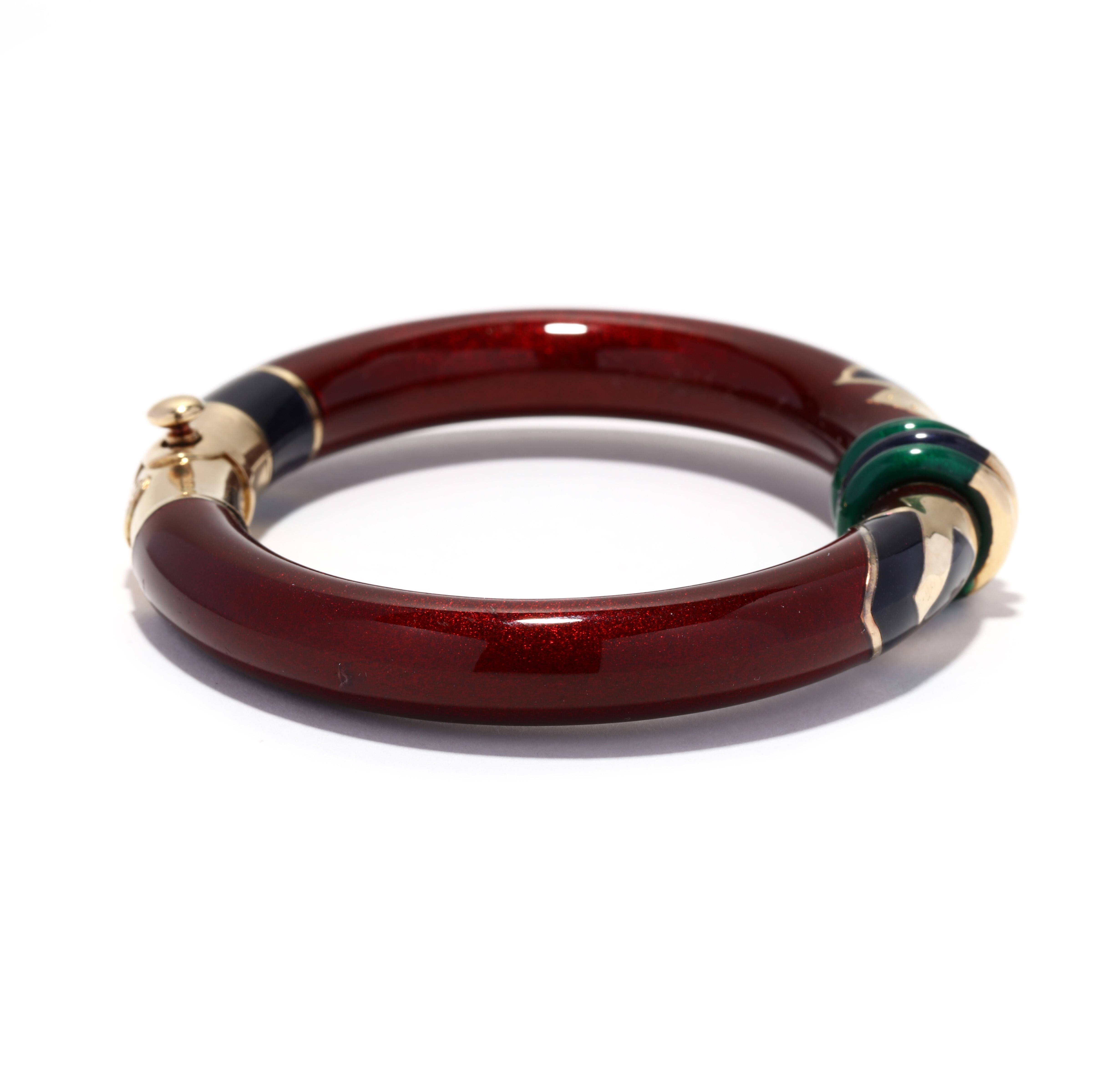 A vintage 18 karat yellow gold, sterling silver, red, green and black enamel bangle bracelet designed by La Nouvelle Bague. This bangle features a red enamel tube with black and green geometric designs and with three enamel rondel beads in the