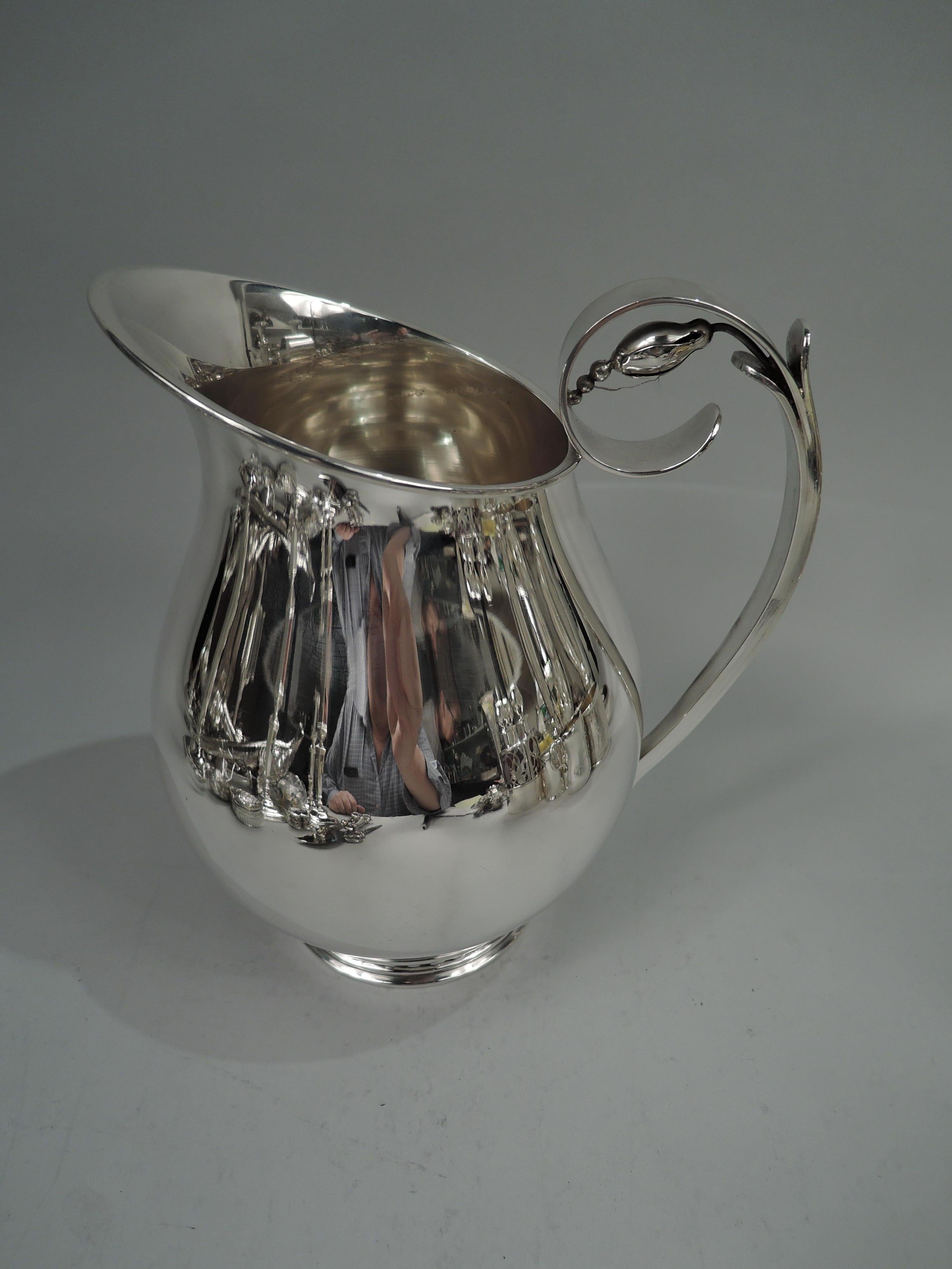 Midcentury Modern sterling silver water pitcher. Made by International Silver Co. in Connecticut. Baluster with asymmetrical oval mouth; stepped and round foot ring with flat beading. High-looping handle with wrapped with abstract leaves; scroll
