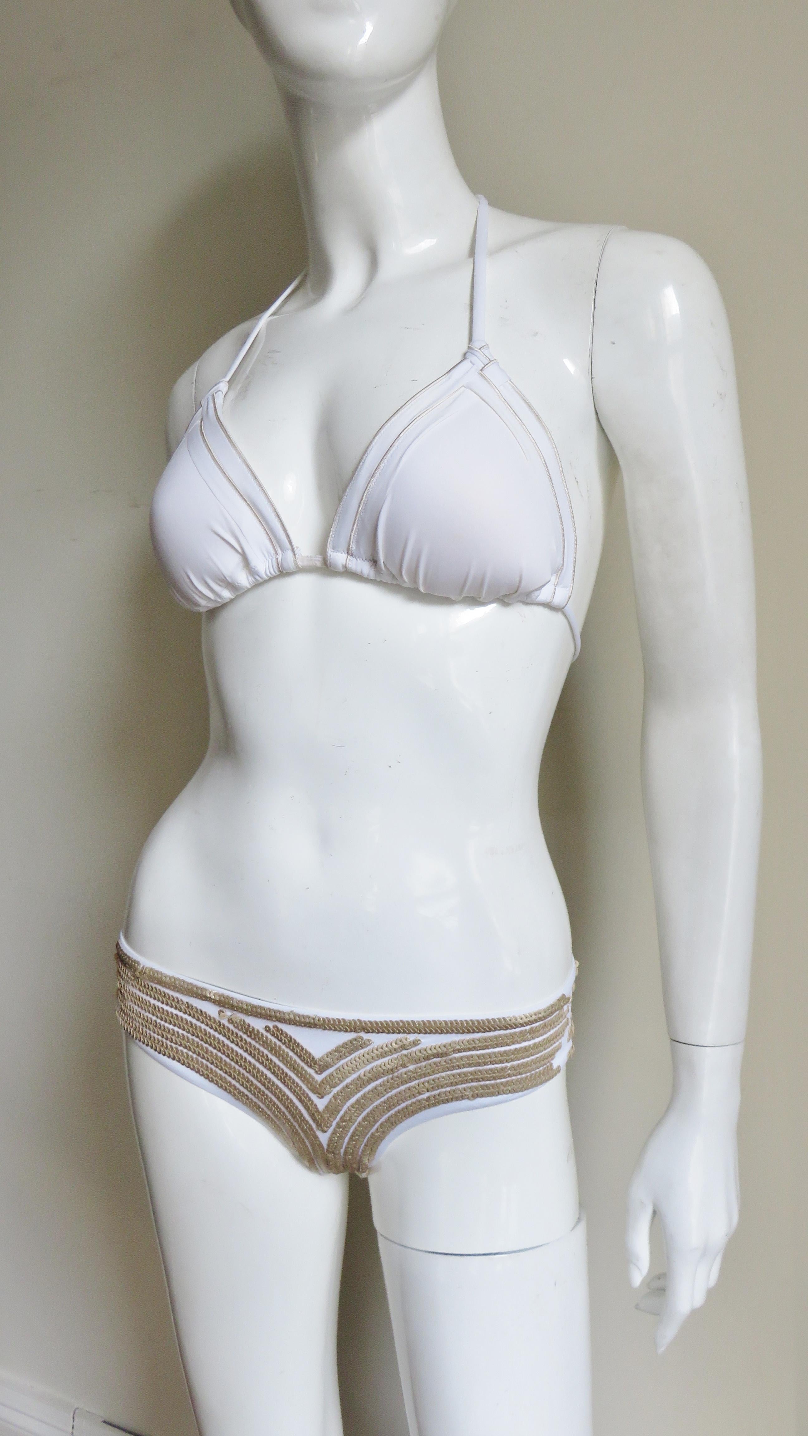 A gorgeous La Perla bikini in white with gold sequins.  The bottoms have an intricate pattern of gold sequins on the front, the back is unadorned solid white.  The top has gold stitching detail, ties at the back and neck and has removable molded