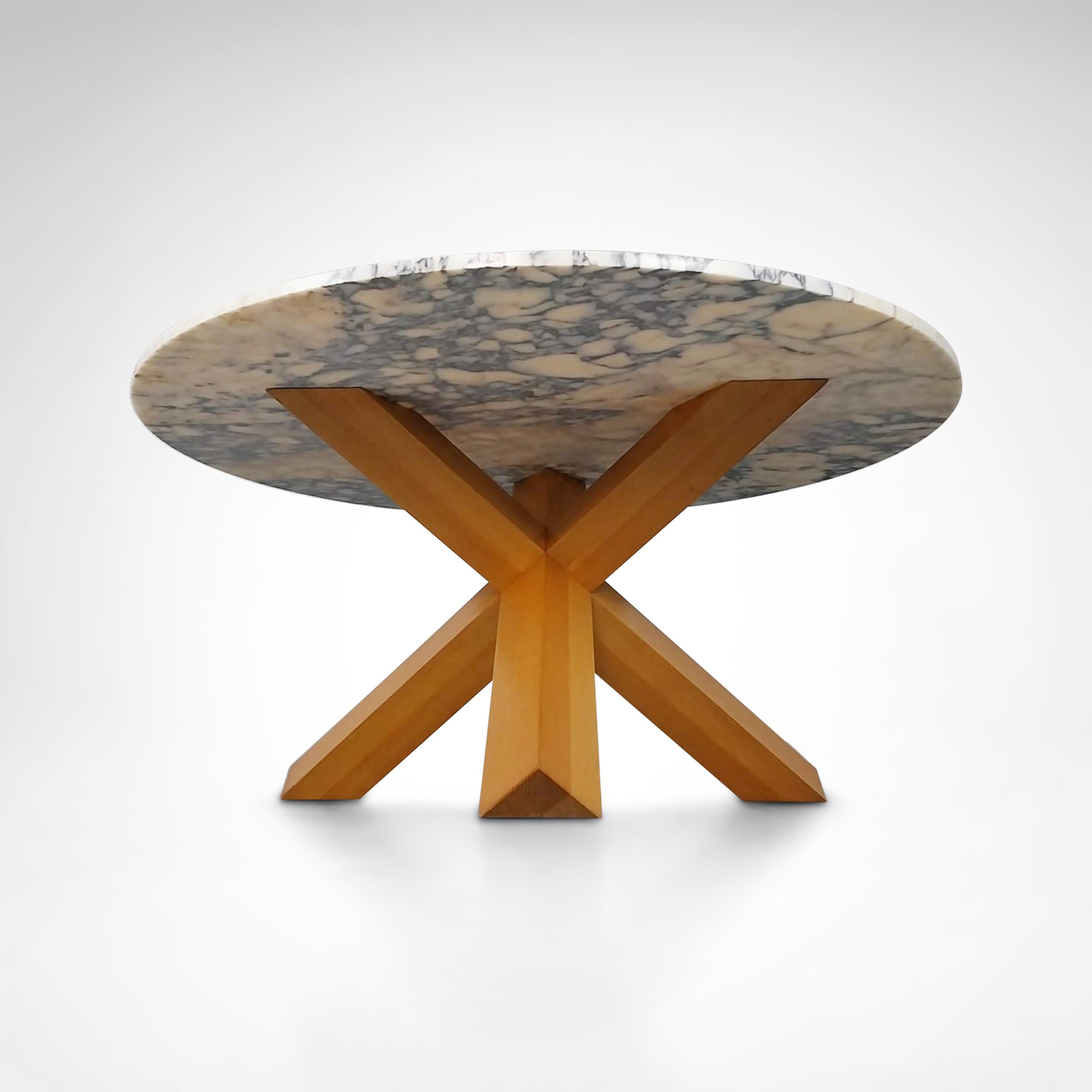 The La Rotonda table designed by Mario Bellini in 1976 has a simple sculpted base, a diag­o­nal inter­sec­tion of three legs with a square cross-section, which supports a 150 cm Amarante marble top, bound together by strong joints carved directly
