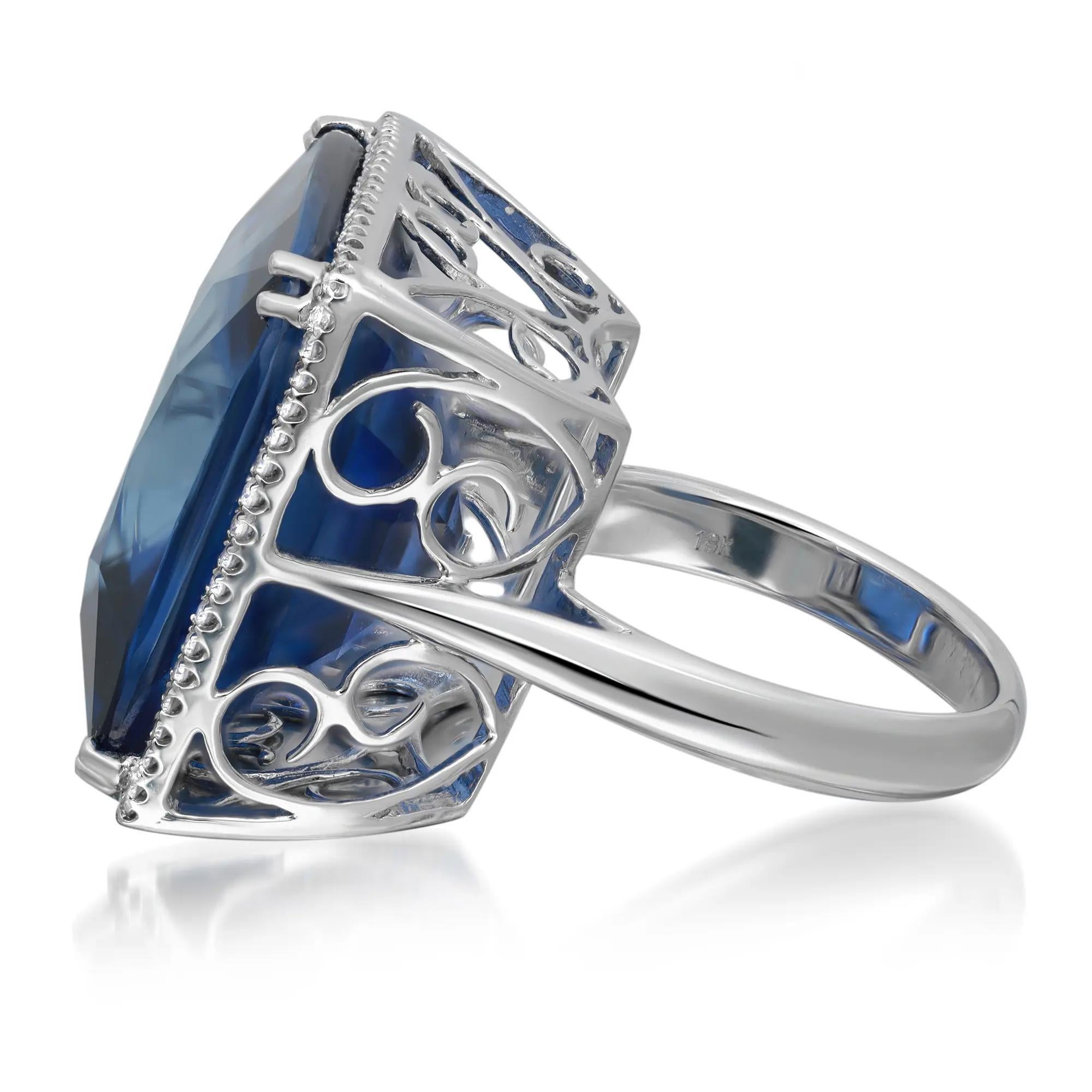 This stunning cocktail ring features prong set square shape synthetic lab created blue sapphire as the center stone with a pave set round natural diamond halo. Crafted in 18K white gold. Total synthetic sapphire weight: 44.54 carats. Total diamond