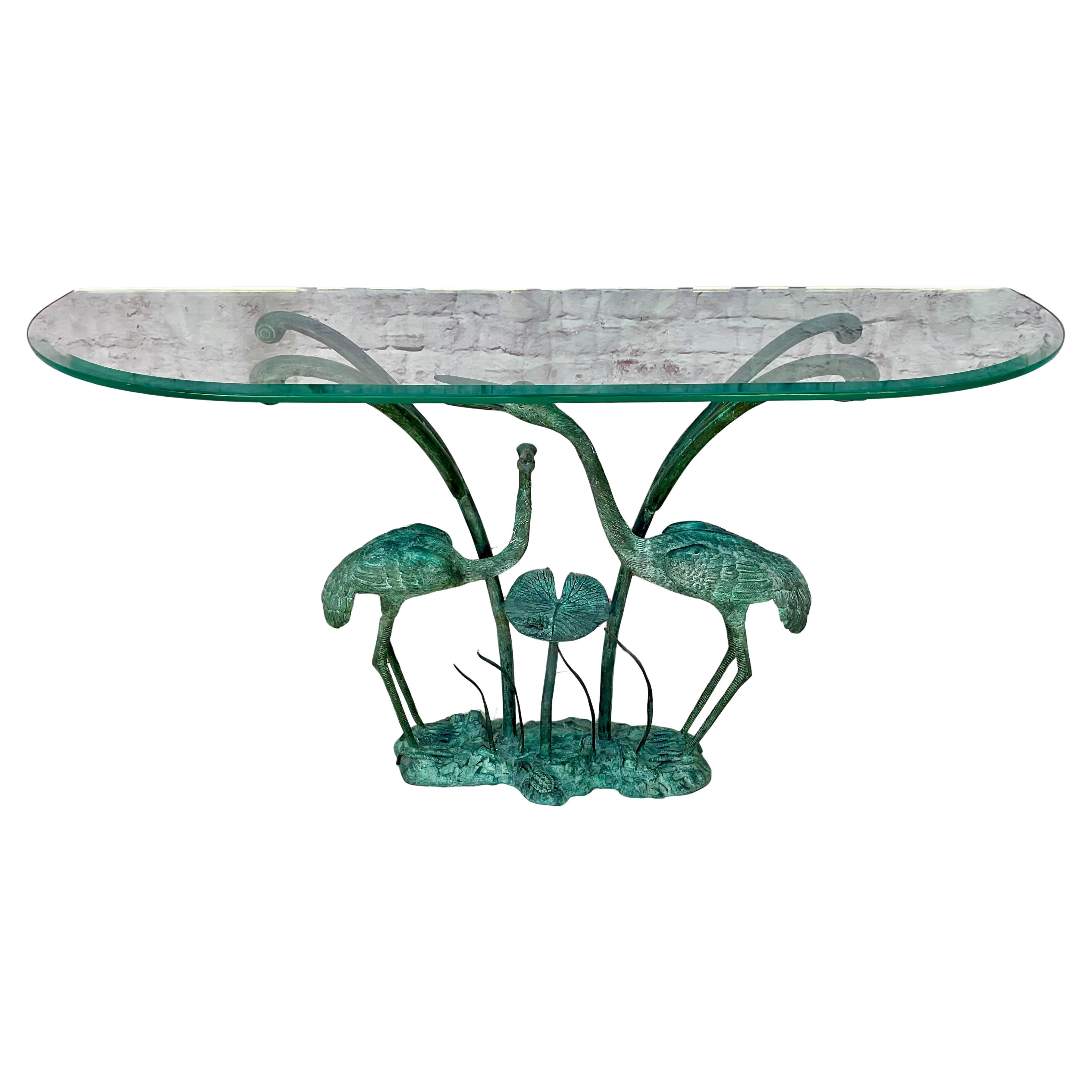 Labarge Bronze Crane and Lily Pad Glass Top Console Table. Glass top is demi-lune shape and allows the intricate base to remain visible. Table features bronze base with two cranes, a frog on a lily pad, and a turtle resting under the cranes. Cranes