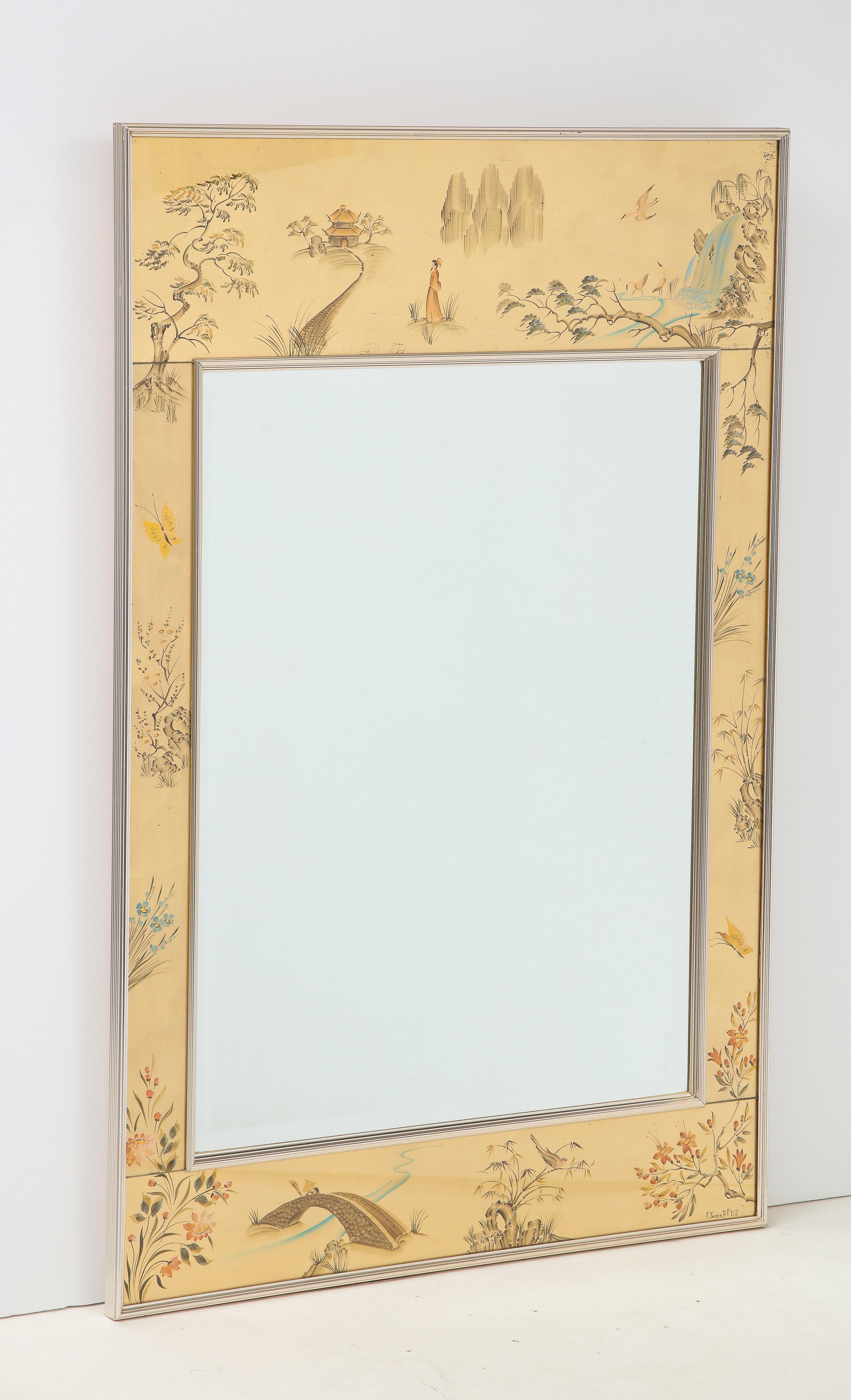 Miroir de style Chinoiserie avec des panneaux en églomisé à la feuille d'or représentant diverses scènes de nature avec flore et chutes d'eau. Les panneaux entourent un miroir biseauté au centre, le tout dans un cadre métallique.