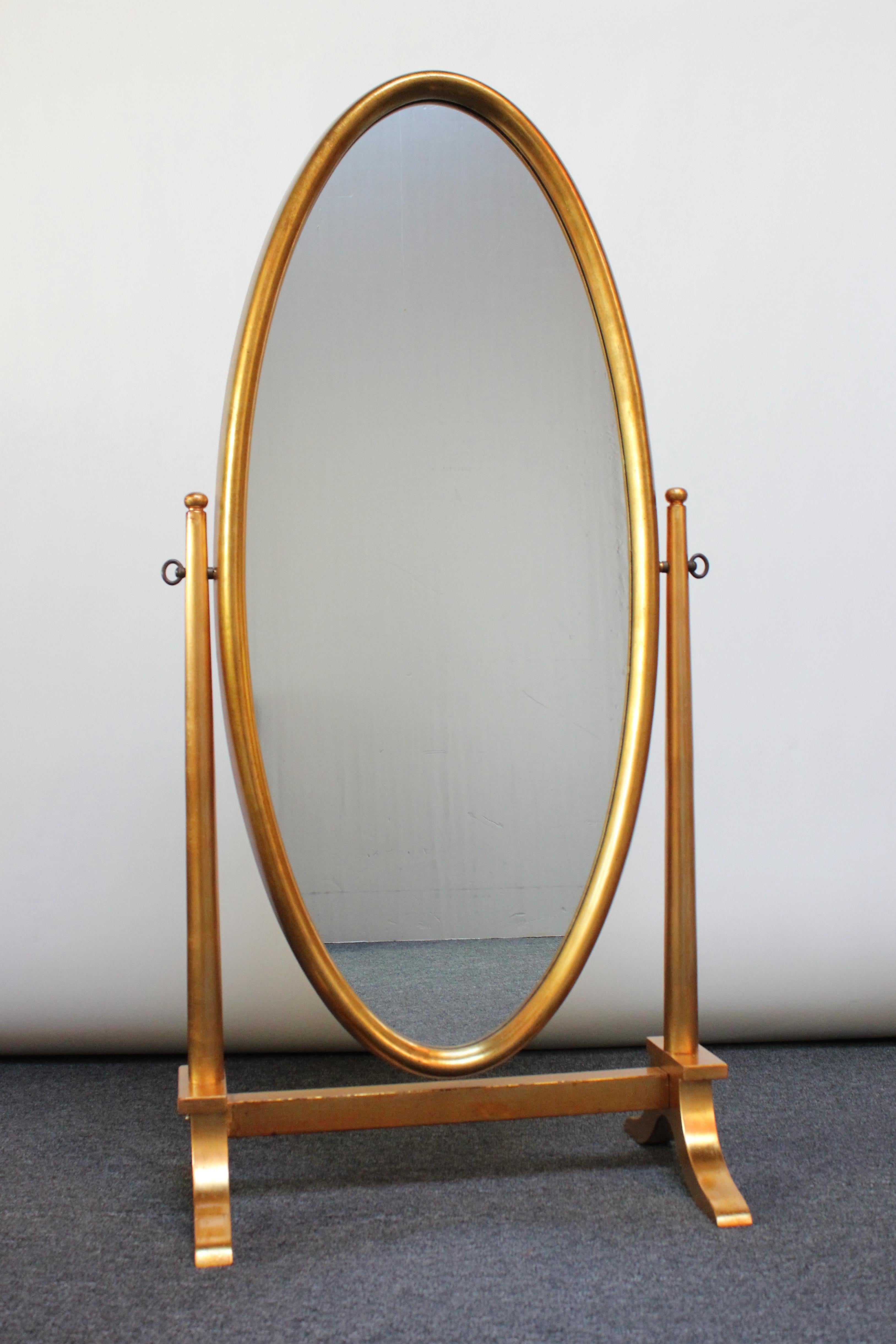 Labarge giltwood cheval floor mirror featuring oval inset glass within a deep, giltwood frame attached to a pedestal base. Mirror can be rotated anywhere along a 360 degree axis and held in place by tightening the keys on either side of the stand.